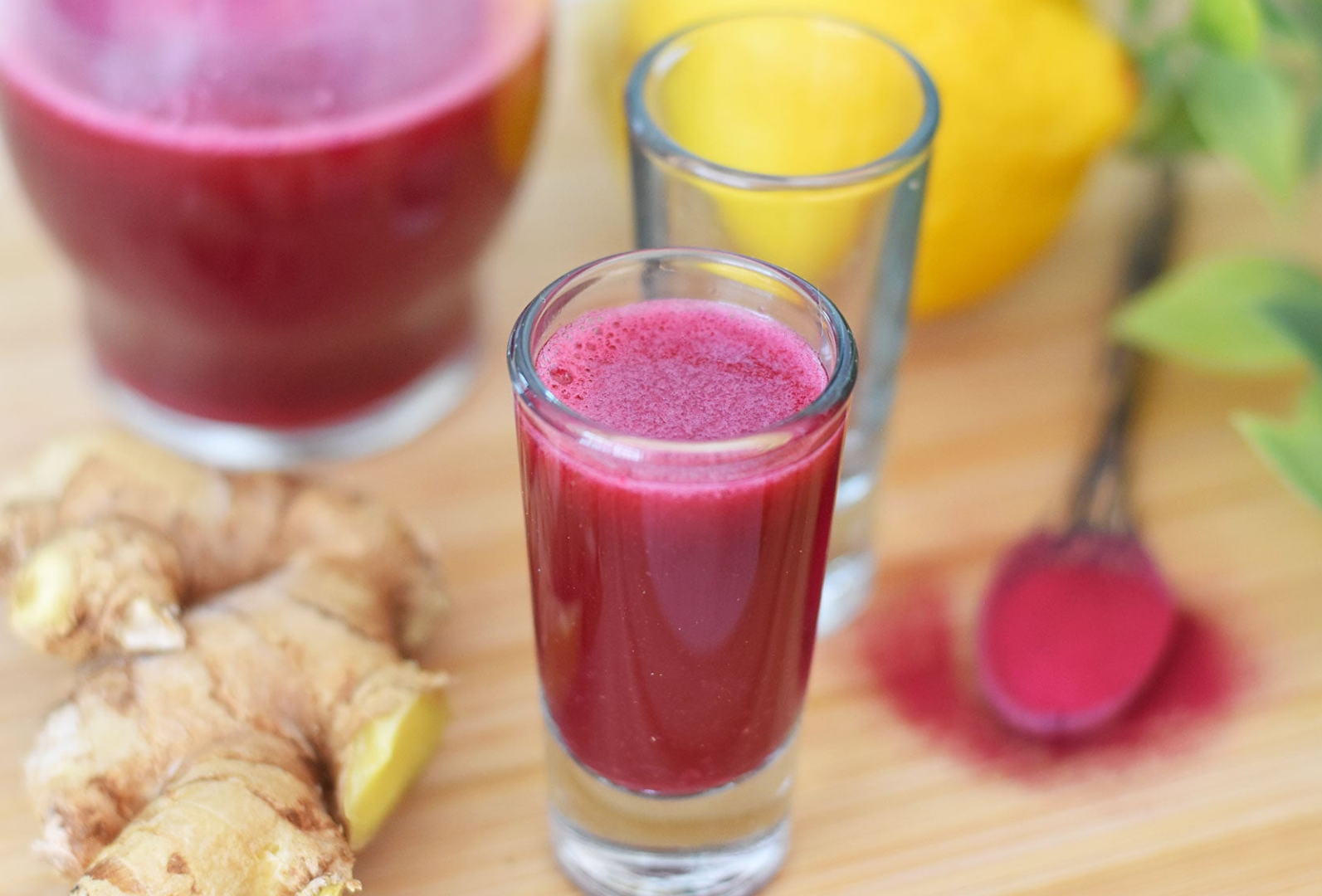A shot glass filled with a red liquid is sitting on a wooden table.