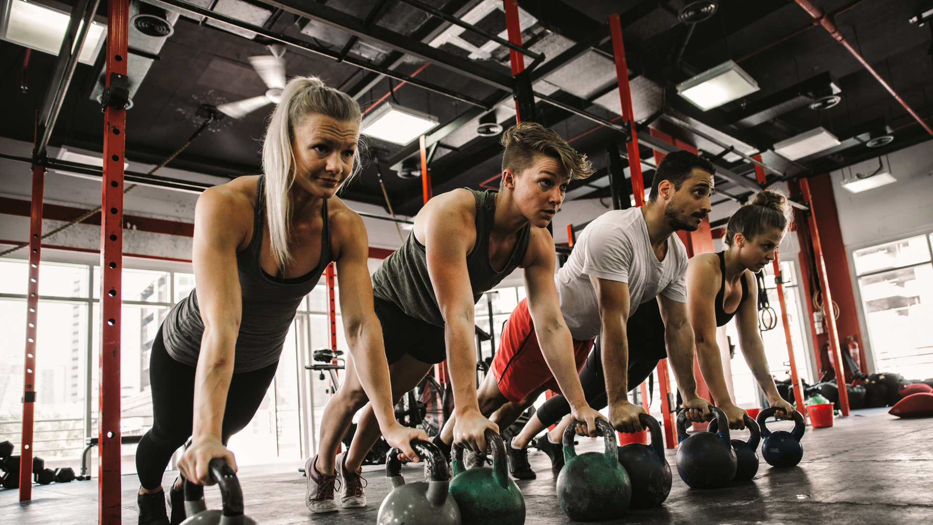 A group of people are doing push ups with kettlebells in a gym.