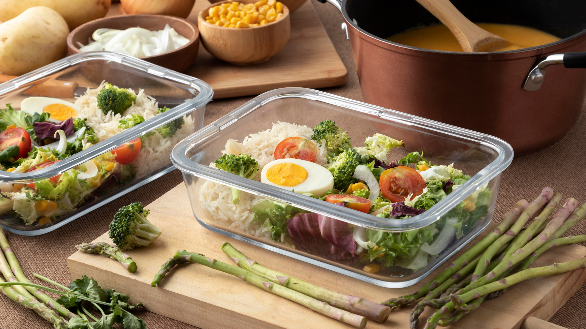 Two glass containers filled with salad, surrounded by vegetables and ingredients.