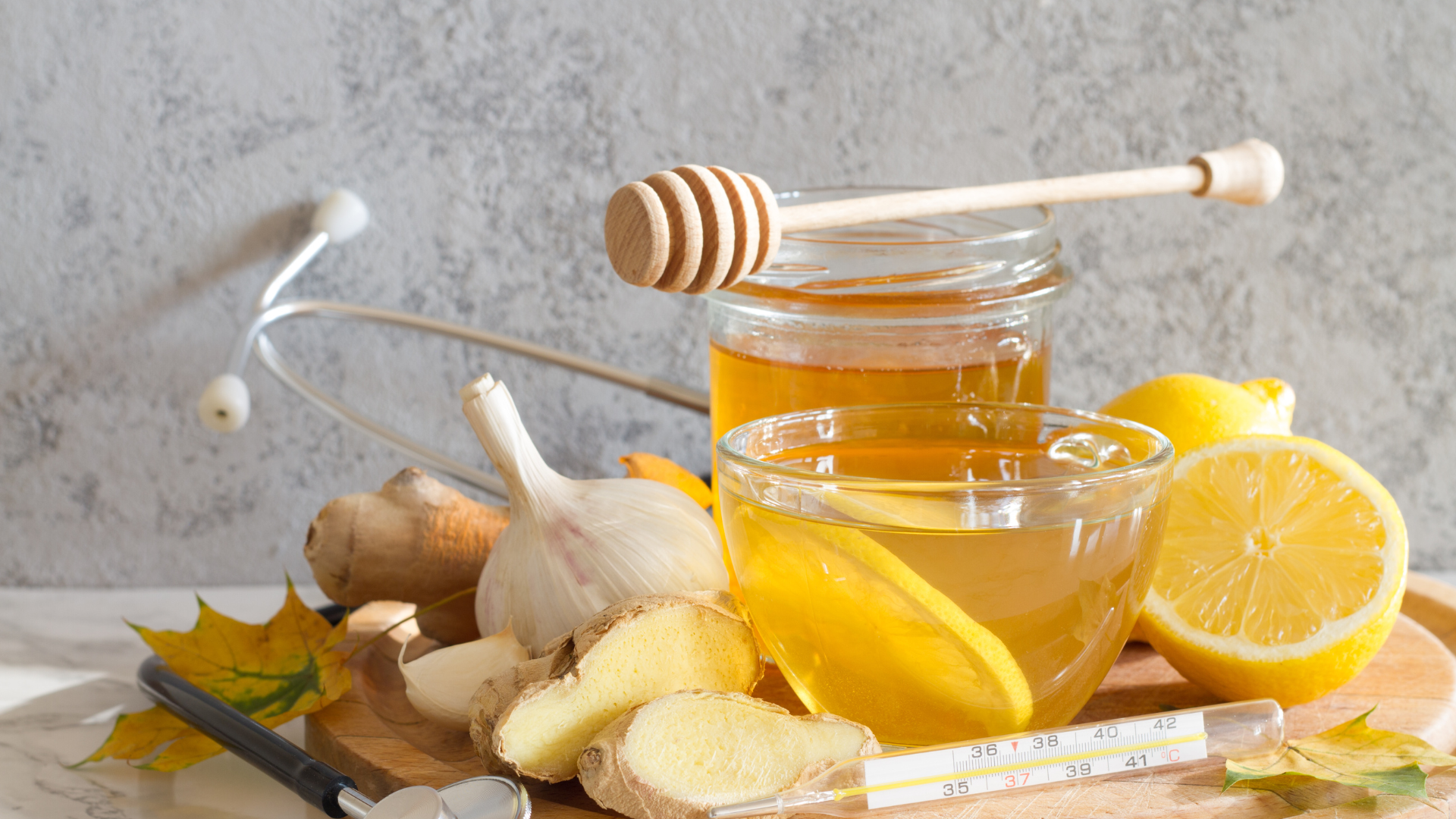 A jar of honey , lemon , garlic , ginger and a thermometer on a cutting board.