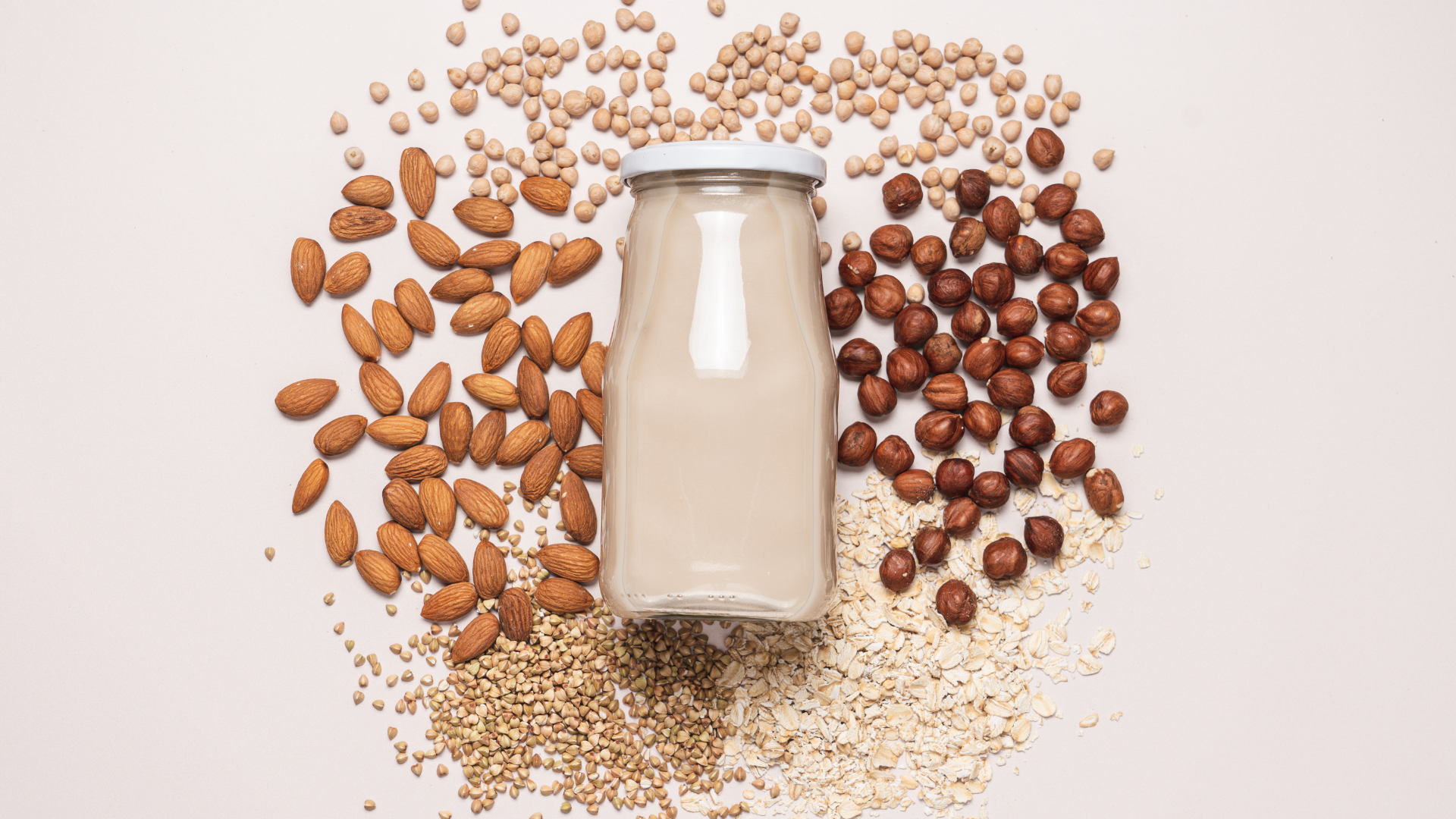 A bottle of milk surrounded by nuts and grains on a table.