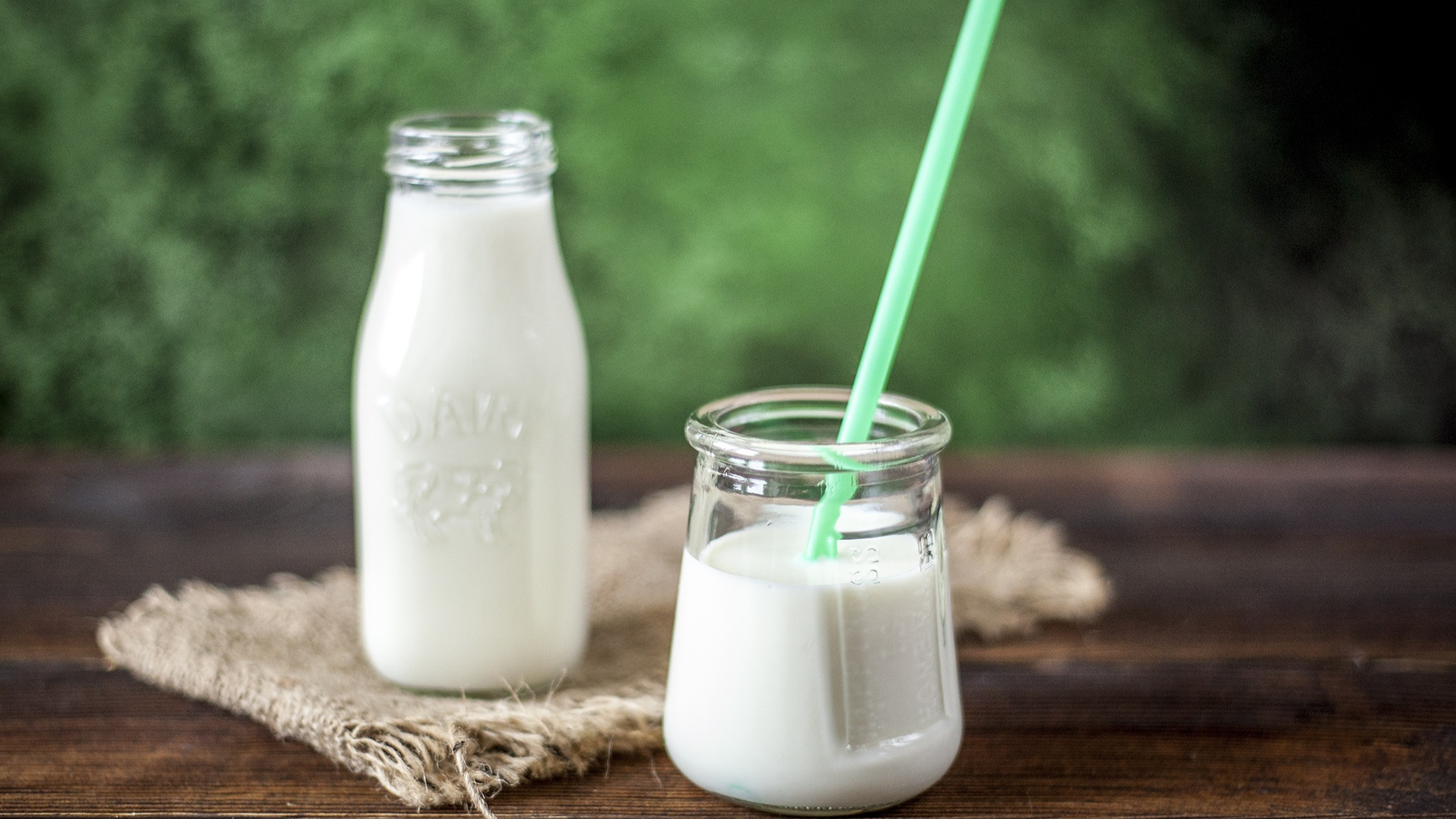 Two bottles of milk and a glass of milk with a straw on a wooden table.