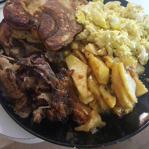 A plate of food with pancakes , eggs , potatoes and meat on a table.