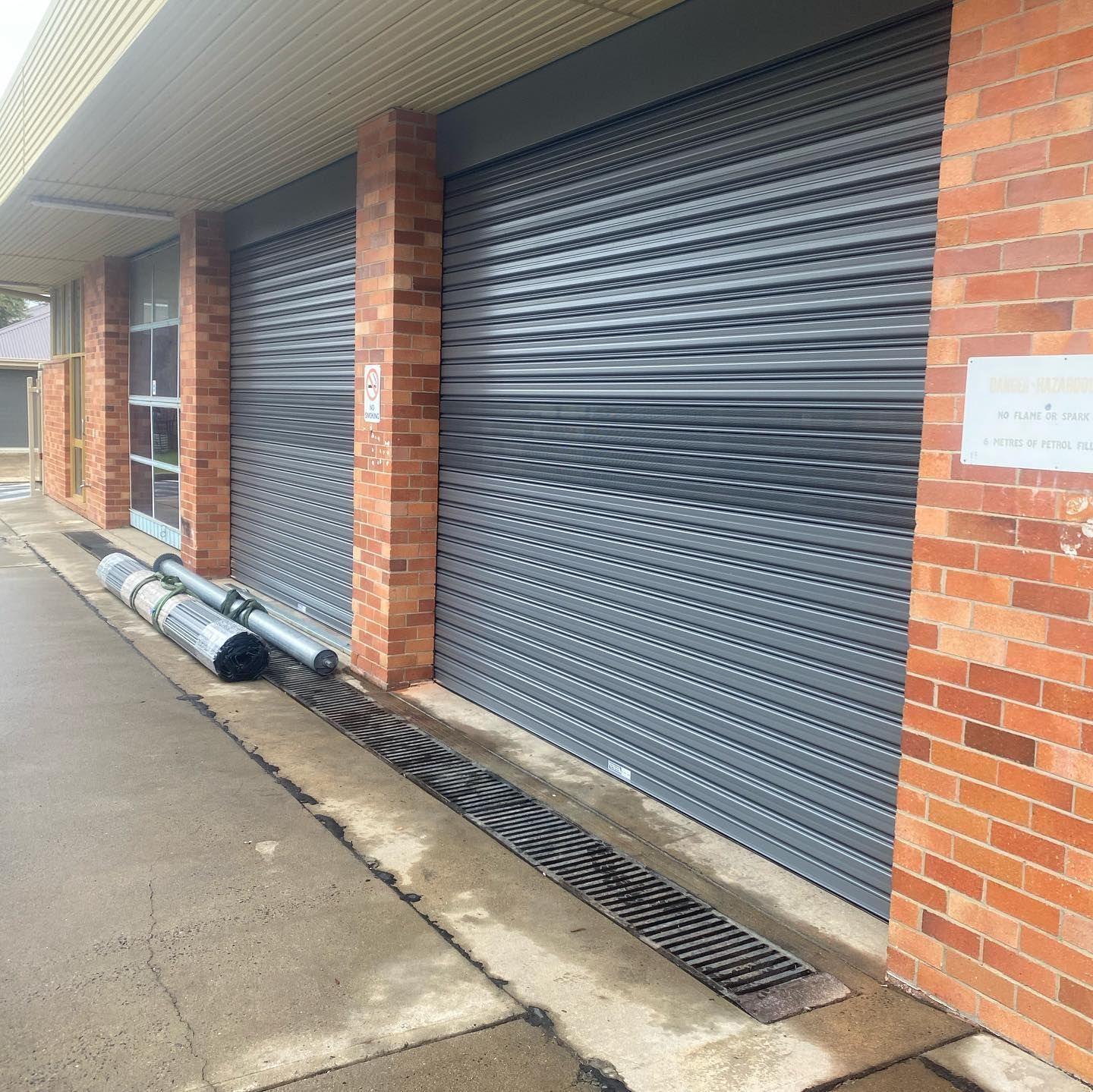 A brick building with a gray garage door and a drain on the sidewalk.
