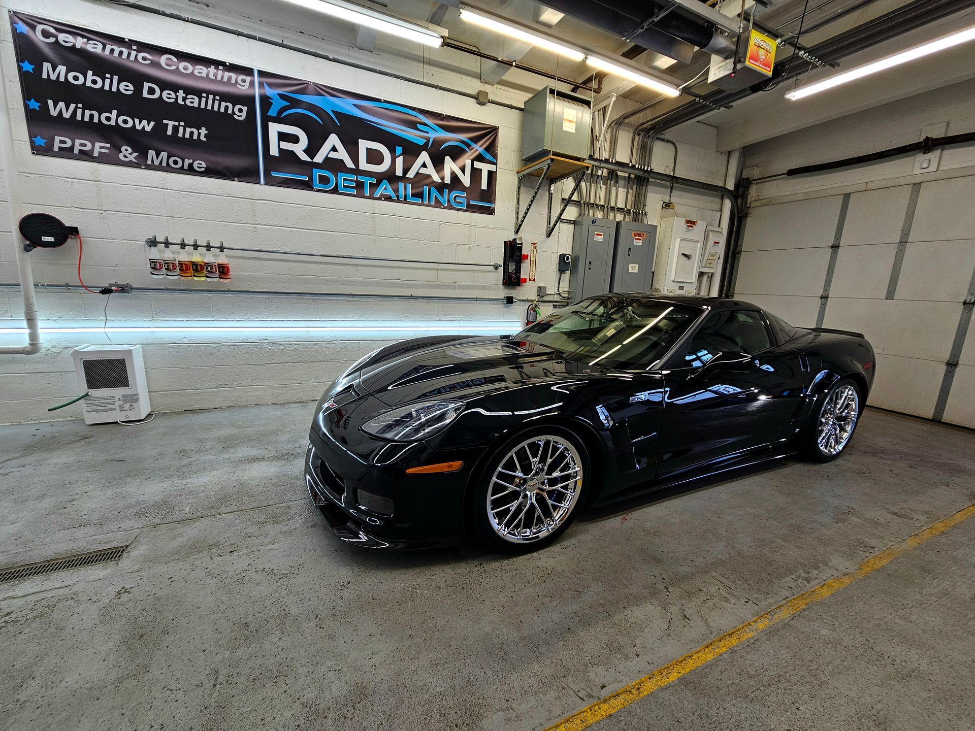 A black sports car is parked in a garage next to a sign that says radiant detailing.
