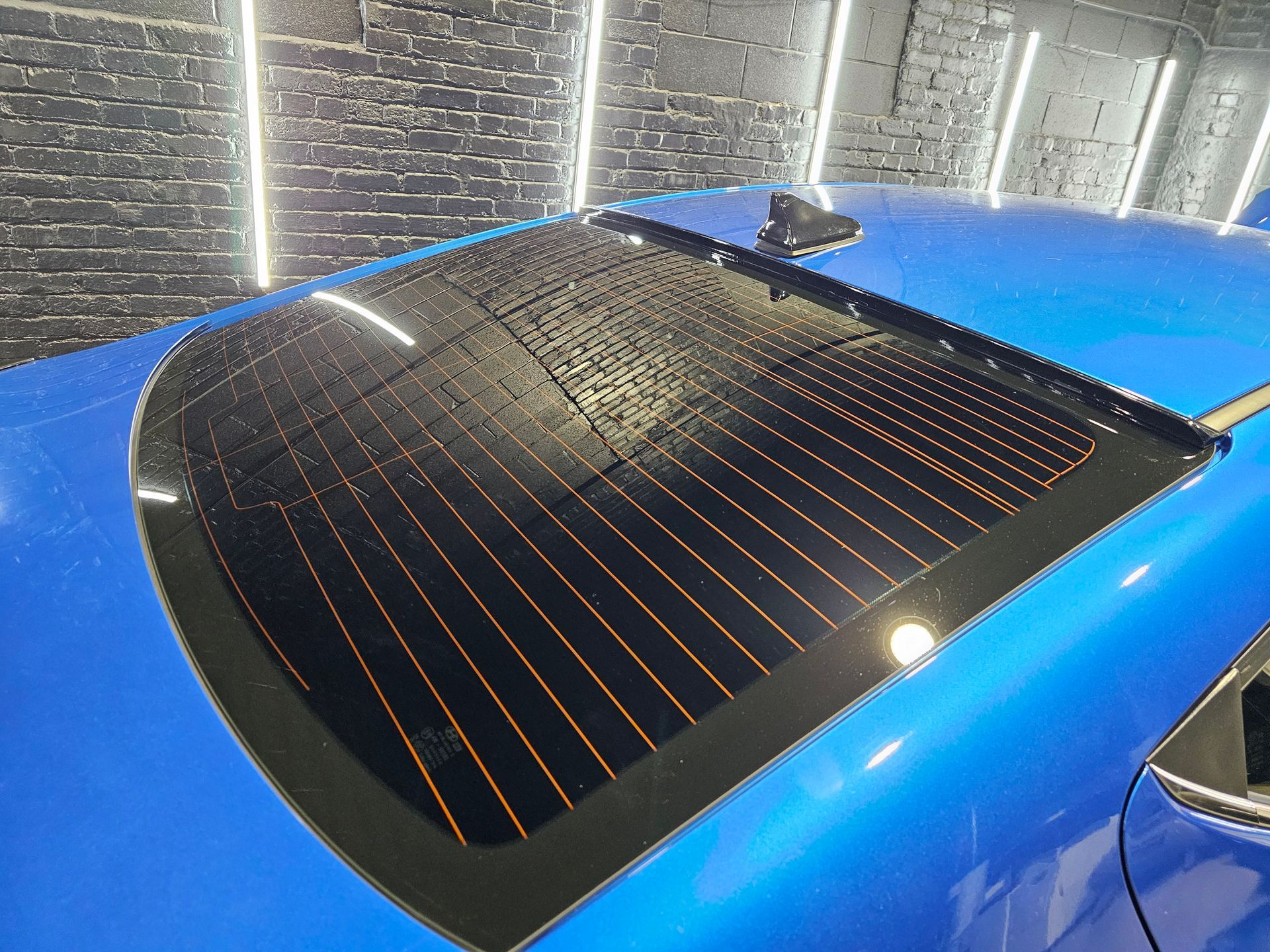 Blue car rear window with black trim, showing heating elements and a defrosted area.