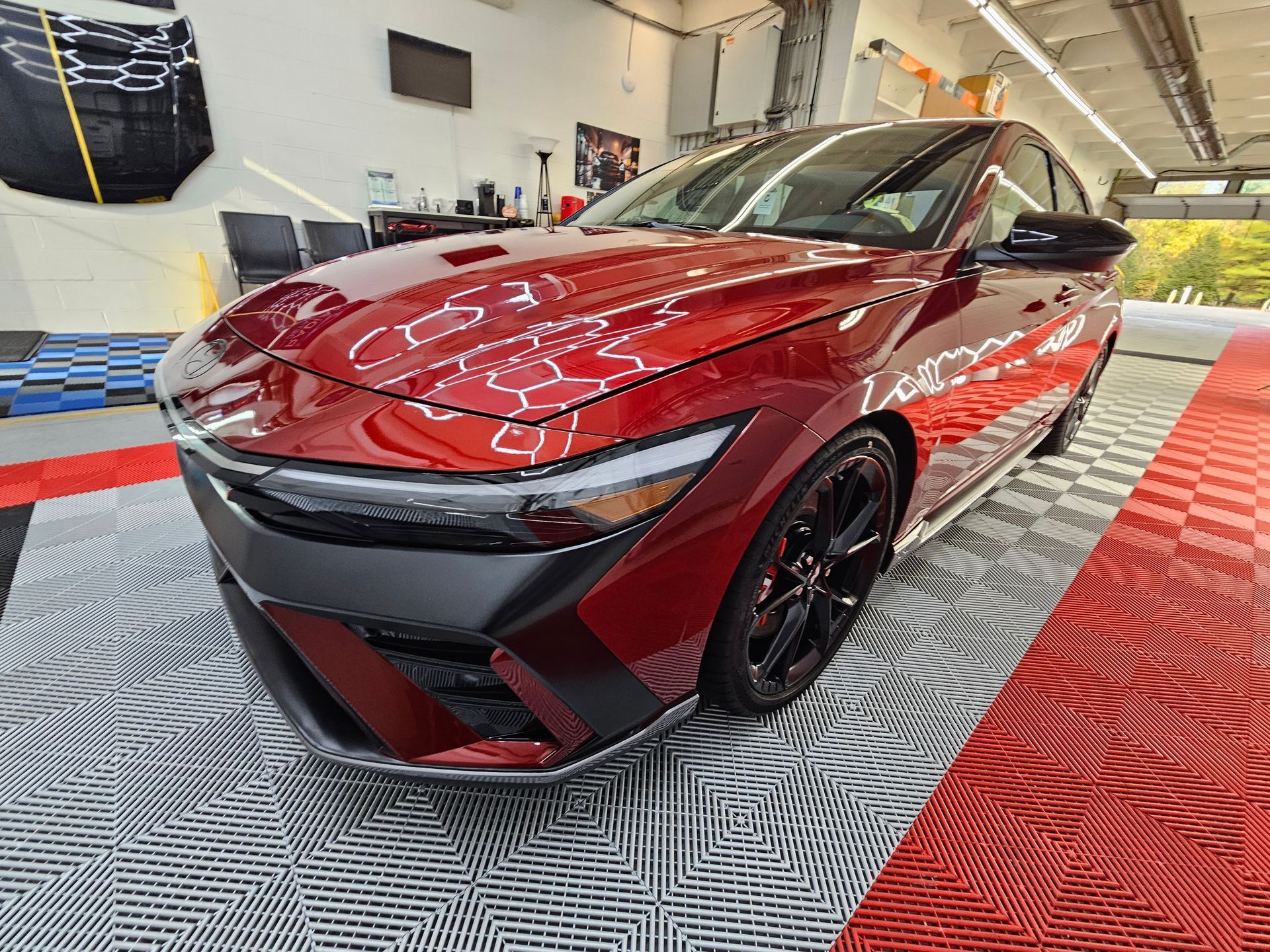 Red car with black wheels parked inside a garage on red and grey patterned flooring.