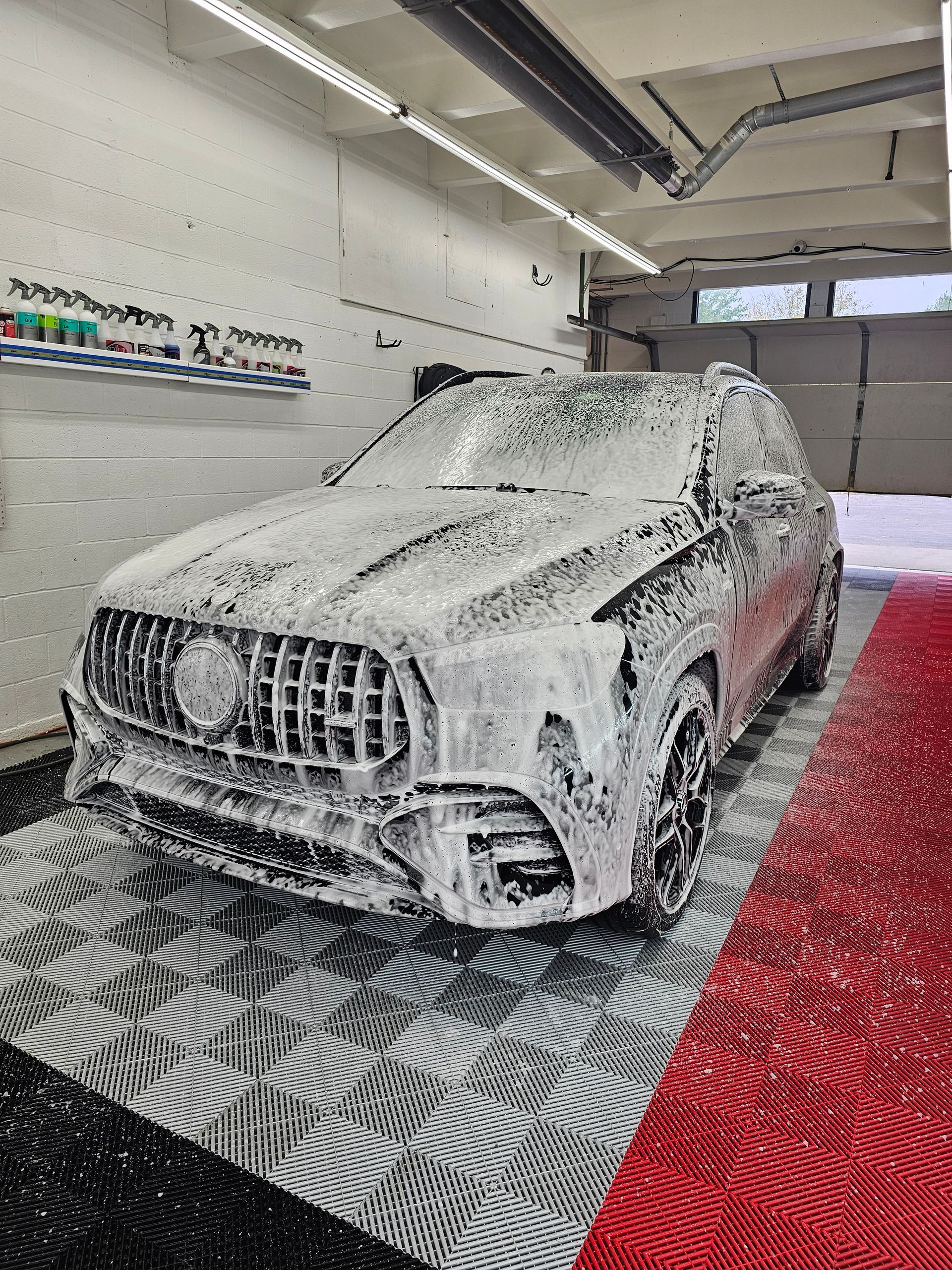 SUV covered in white foam at a car wash. The car is black, and the floor is red and gray.
