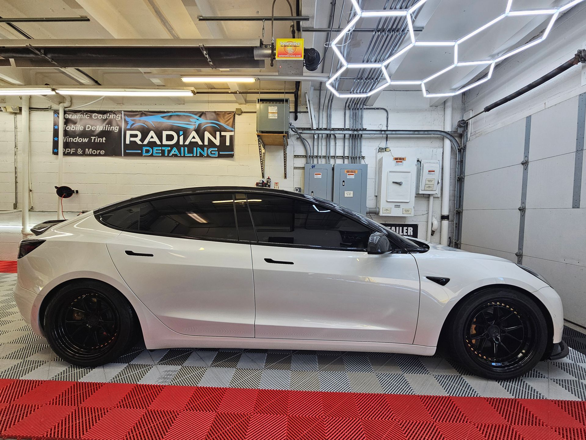 A blue tesla model x is parked in a garage next to an american flag.