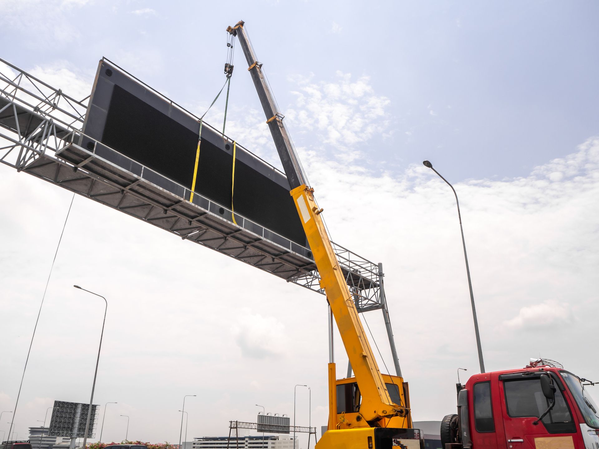 Crane rental lifting LED signboard at construction site with clear blue sky background. Crane rental lifting LED signboard at construction site with clear blue sky background.