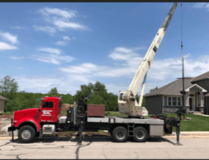 Red crane truck parked on a street, boom extended toward a pole, under a blue sky.