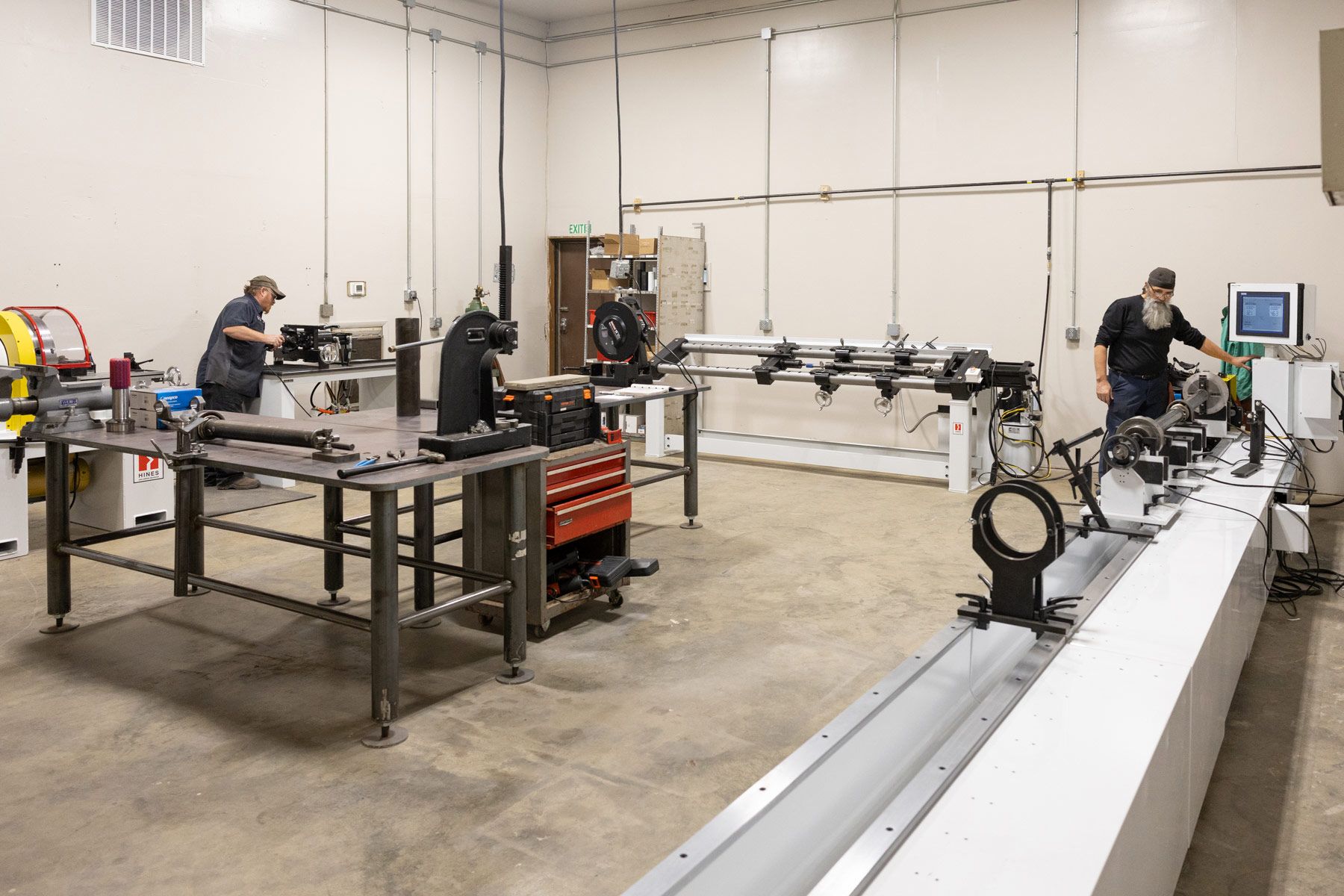 Three people working in a semi repair shop with various driveshaft repair equipment.