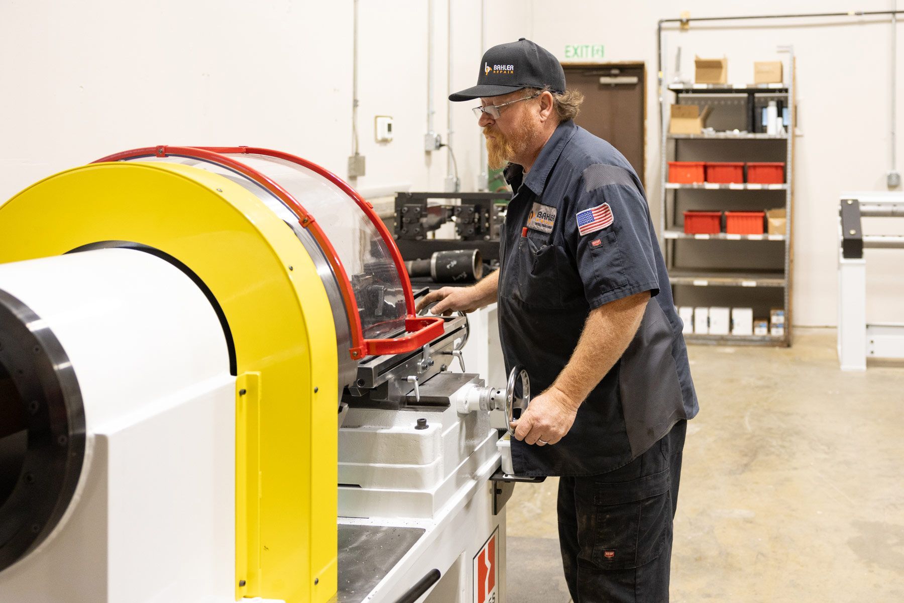 A mechanic works under a lifted semi-truck in a repair shop. Other trucks and equipment are visible.
