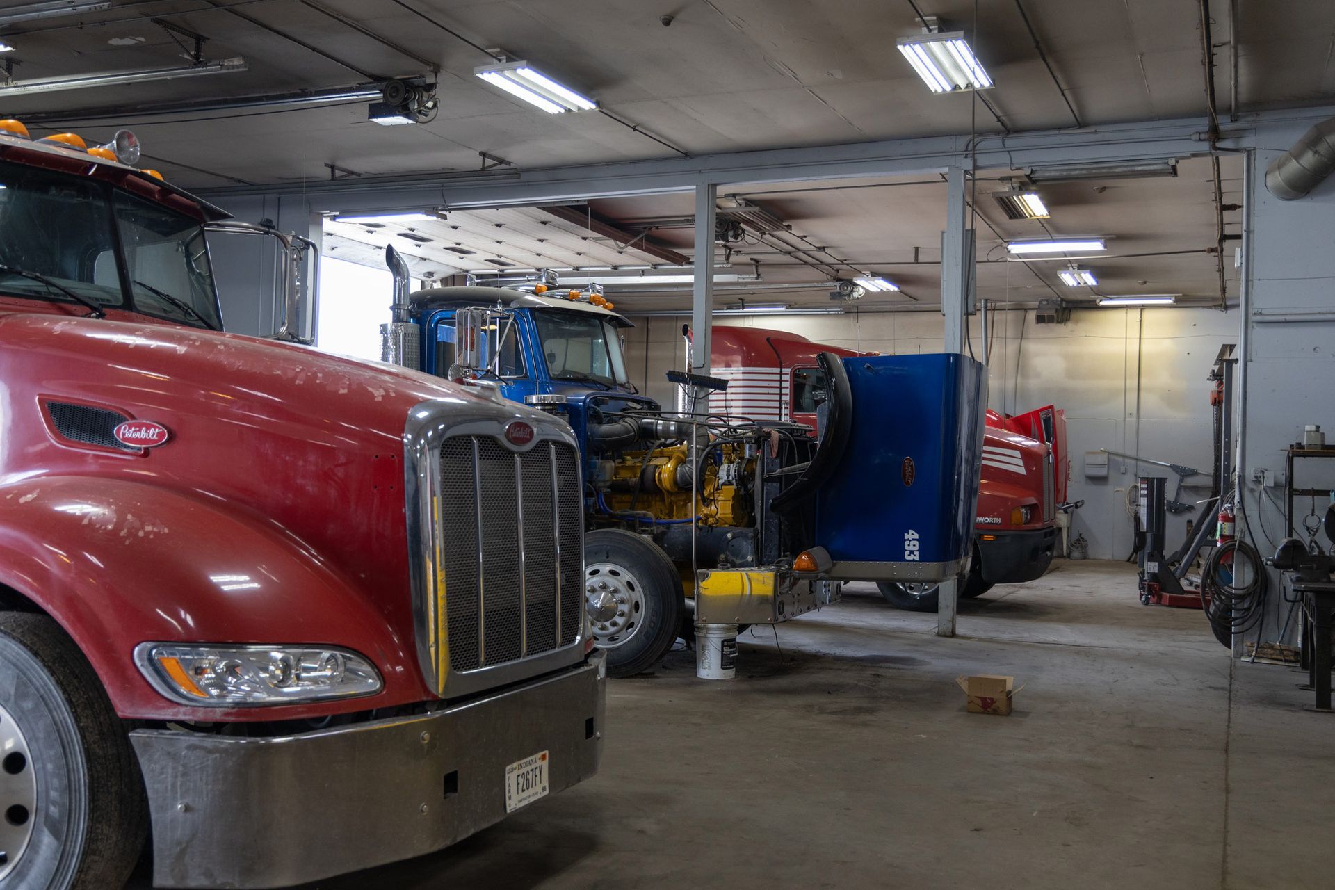A semi-truck repair shop with multiple trucks. A red truck is in the foreground, with other trucks and equipment visible in the background.