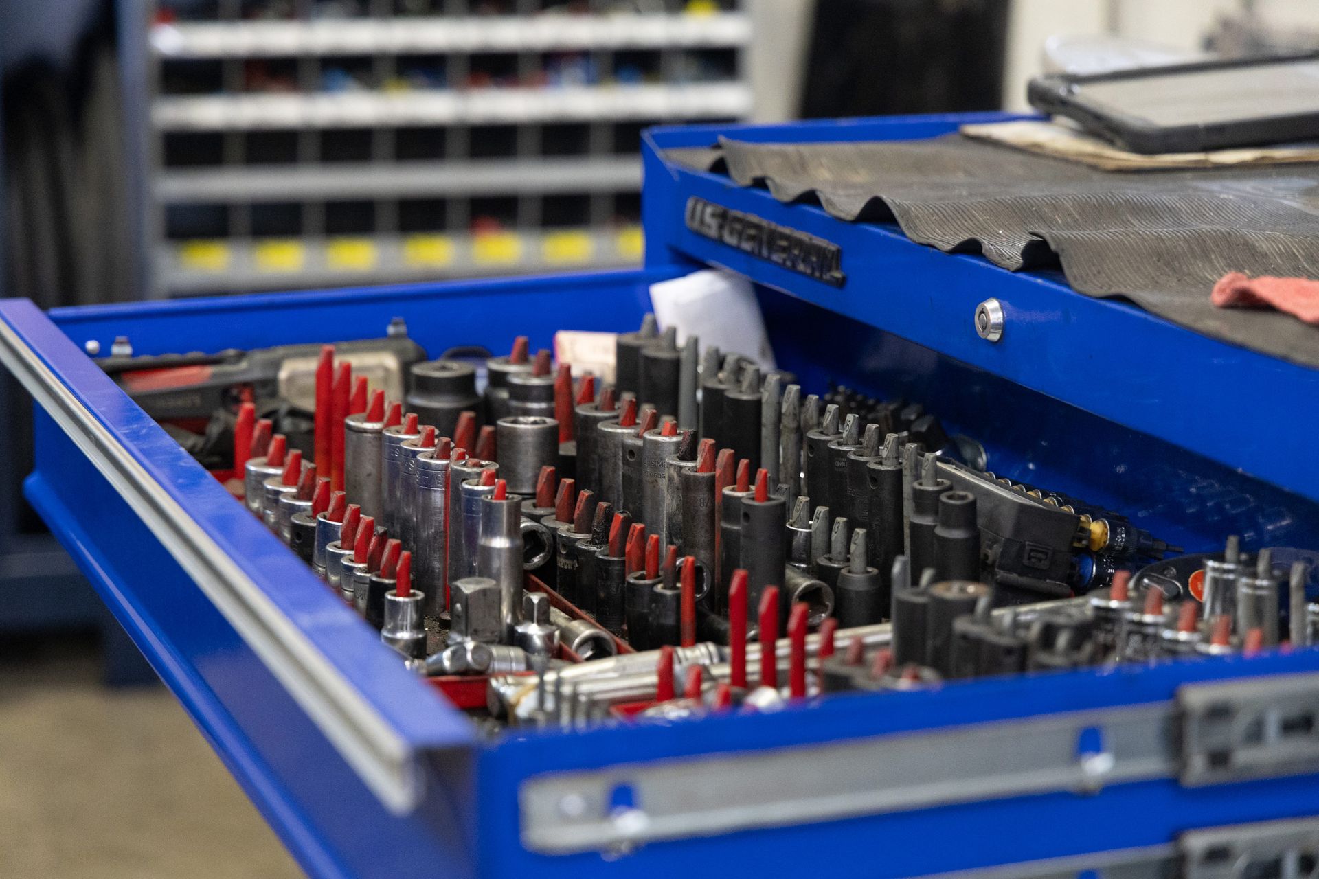 Blue toolbox drawer filled with organized tools, including sockets and wrenches, in a workshop setting.