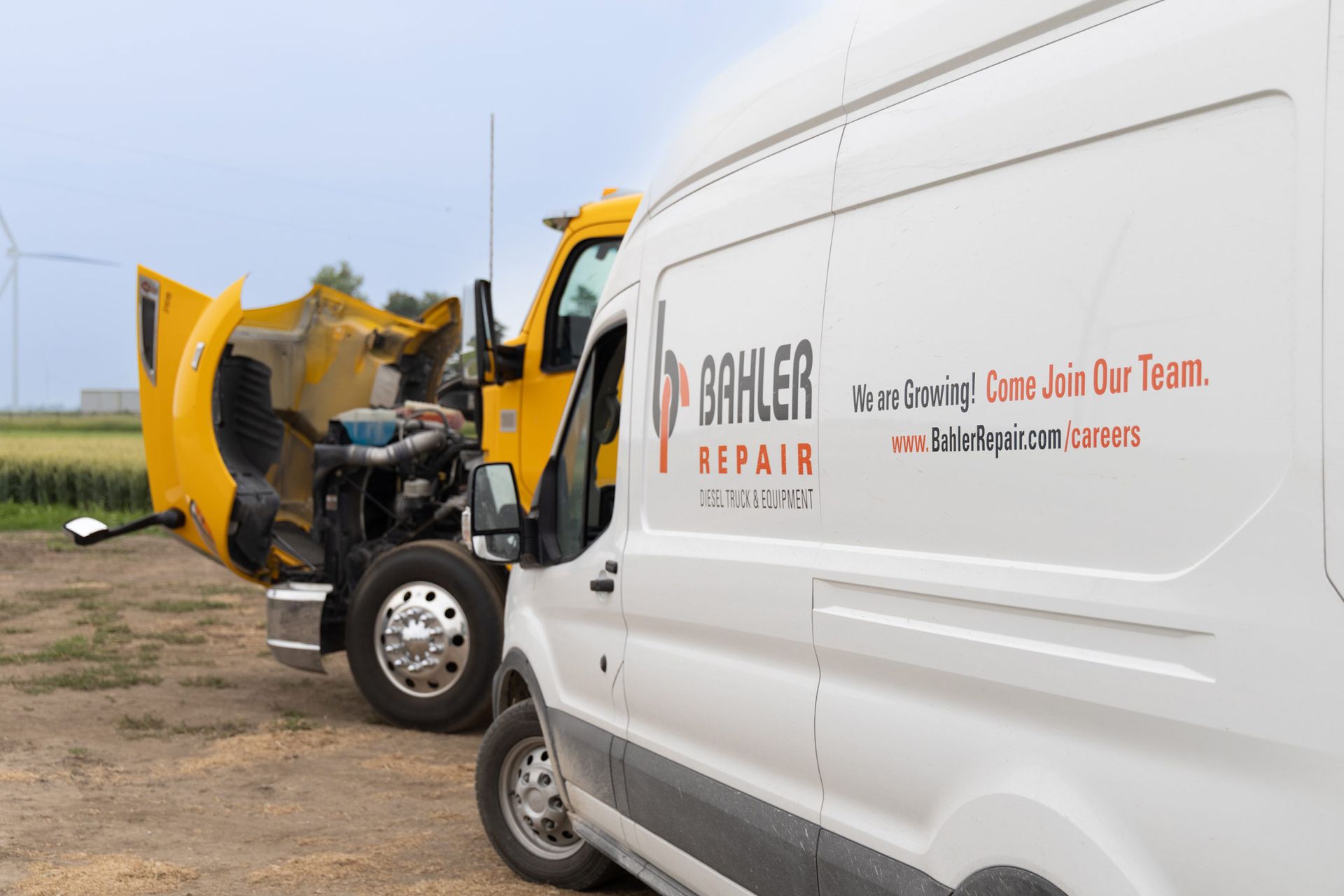 A yellow semi-truck with its hood open next to a white van with 