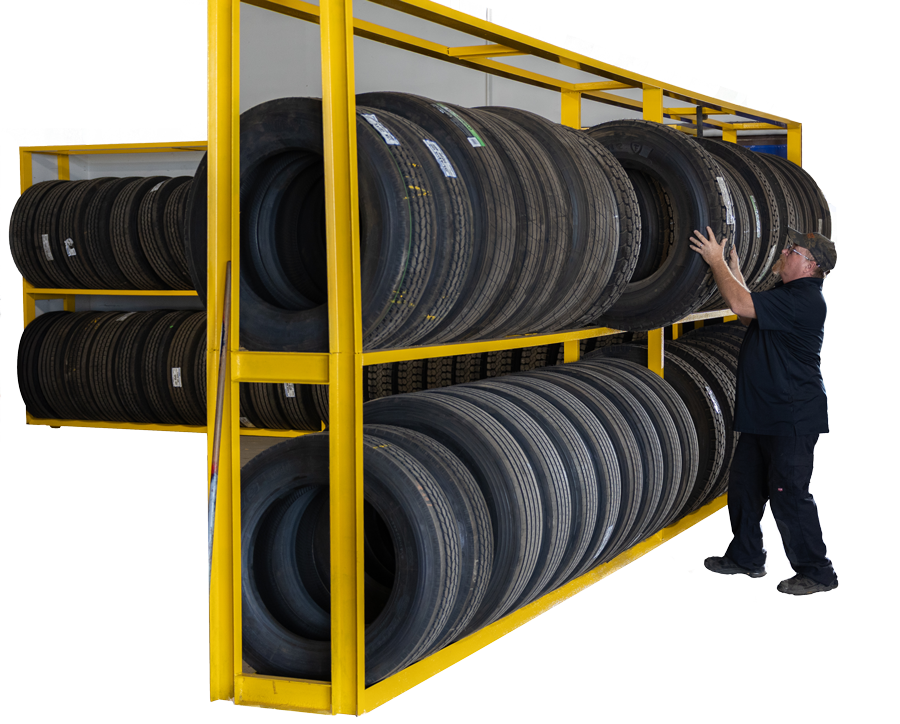 A person placing a tire on a yellow rack filled with many tires in a garage setting.