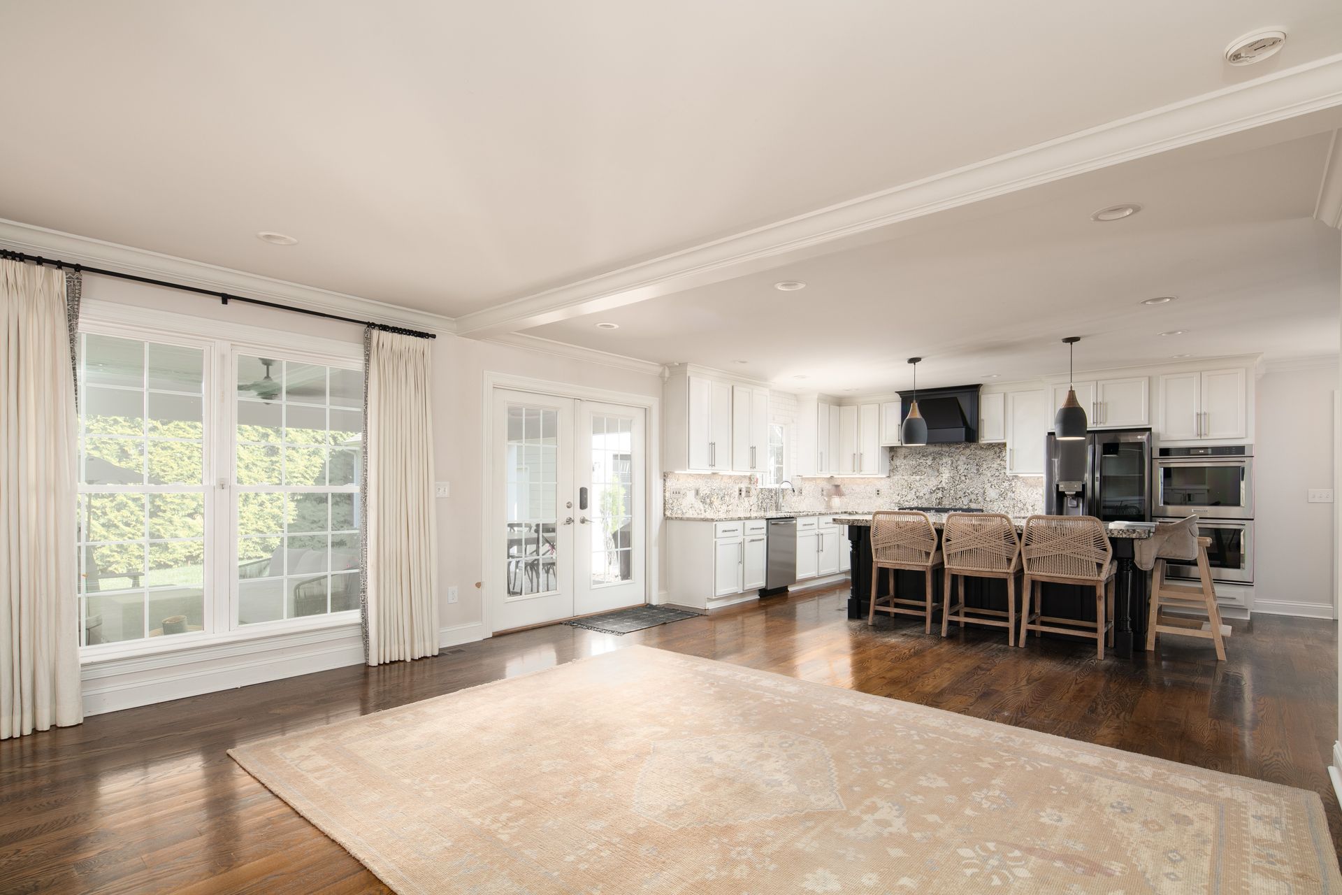 Open-concept kitchen and living area with hardwood floors, a large beige rug, glass doors, and a kitchen island with stools.