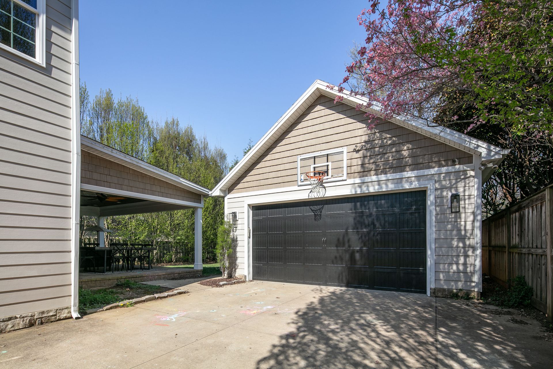 A two-story house with a covered patio and a detached garage featuring a basketball hoop above the black door.