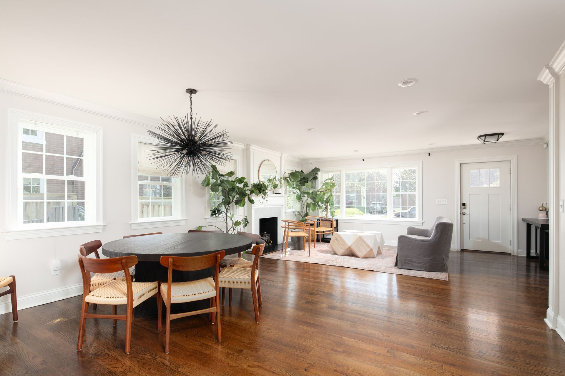 An open-concept dining and living area with hardwood floors, a large dark oval dining table, and a modern chandelier.