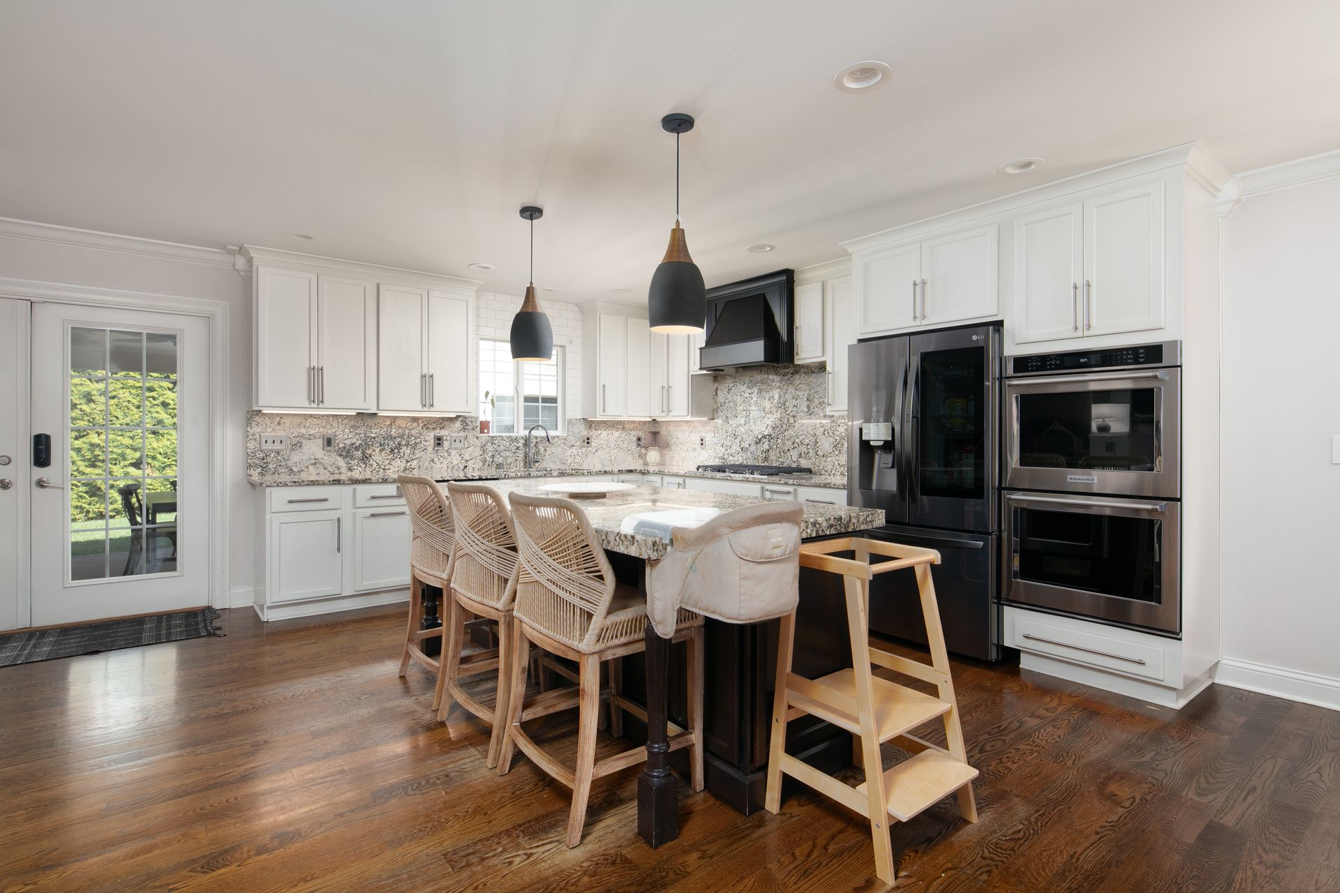 A bright, modern kitchen featuring white cabinets, a black island with wooden stools, stainless appliances, and wood floors.