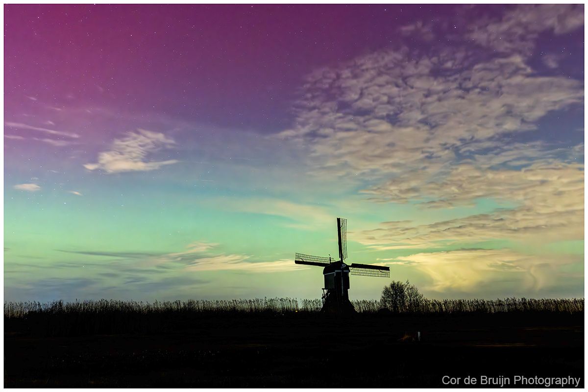 Silhouette of a windmill against a vibrant, multicolored sky at dusk.
