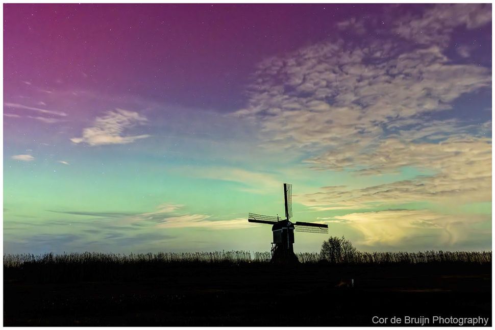 Silhouette of a windmill against a vibrant, multicolored sky at dusk.