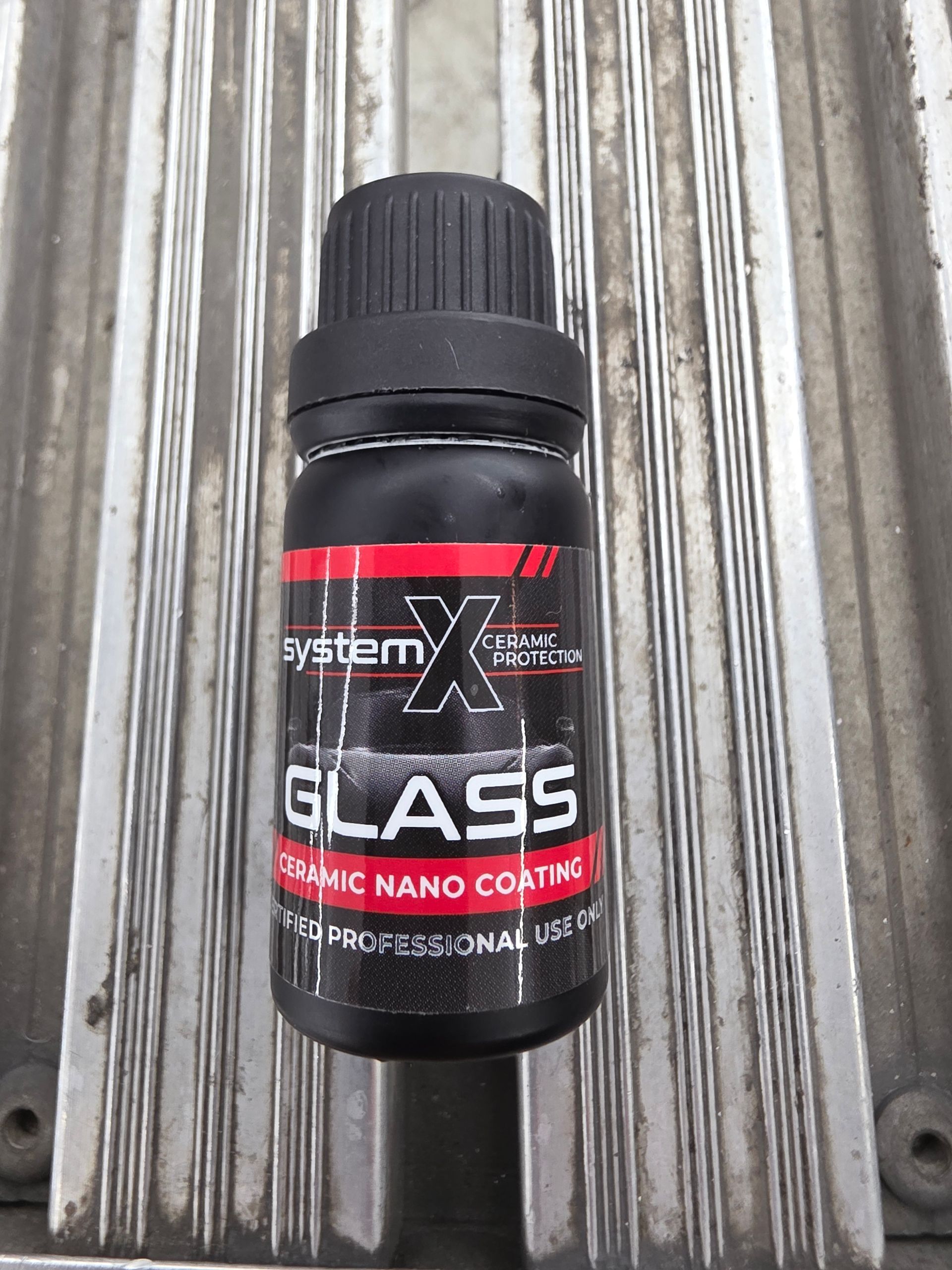 A person wearing black gloves applies a ceramic coating to a white car hood using a small blue applicator block.