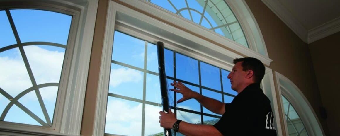 A person installing tinted film onto a large, multi-pane residential window with an arched top.