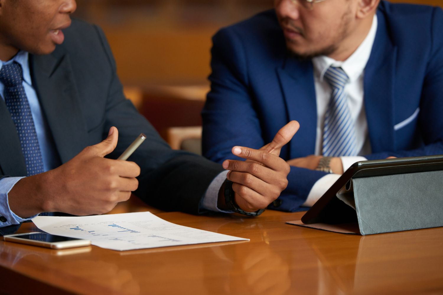 Two businesspeople in suits discussing a document at a conference table with a tablet nearby