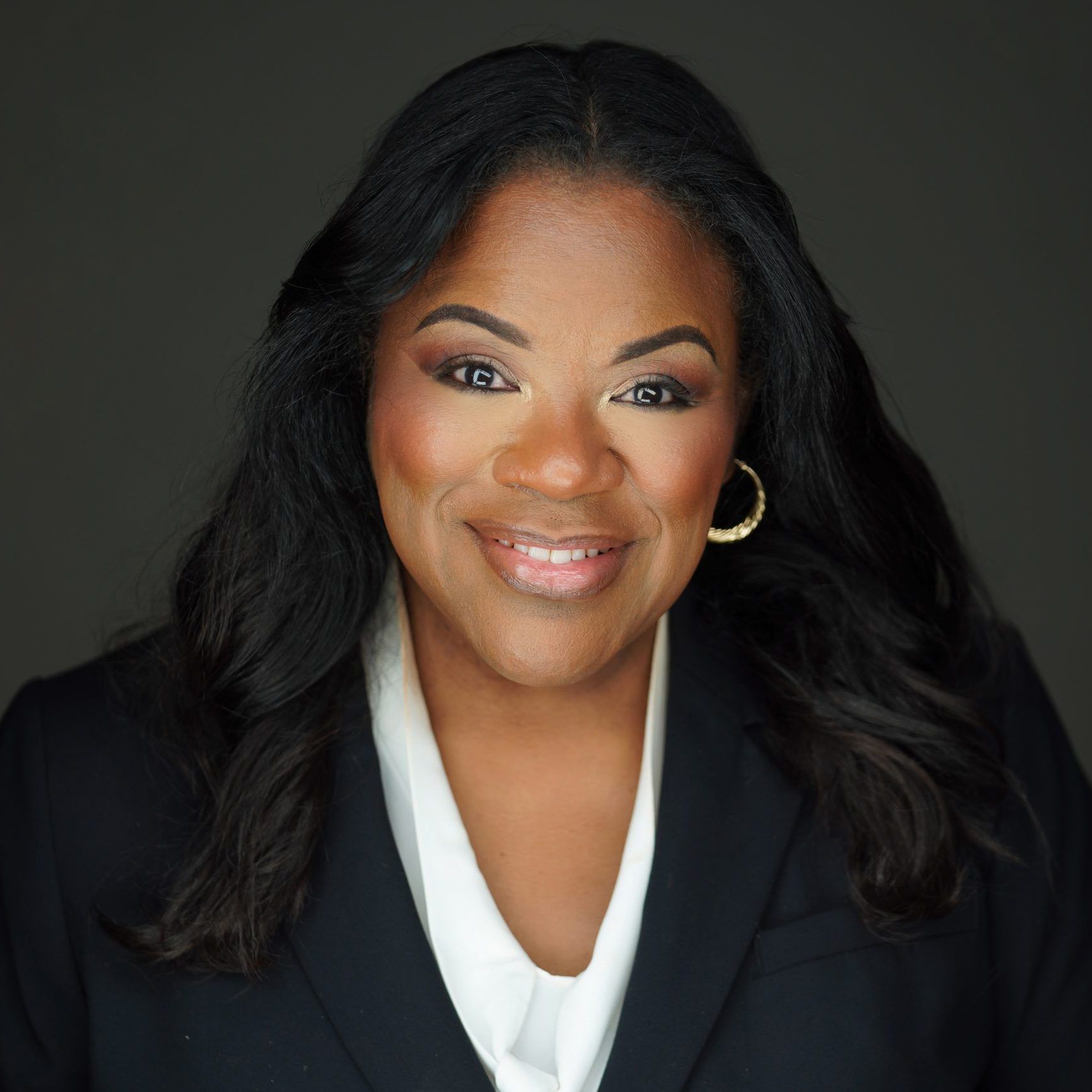 Studio headshot of Lisa Wogwu in a black blazer and white blouse on a dark background