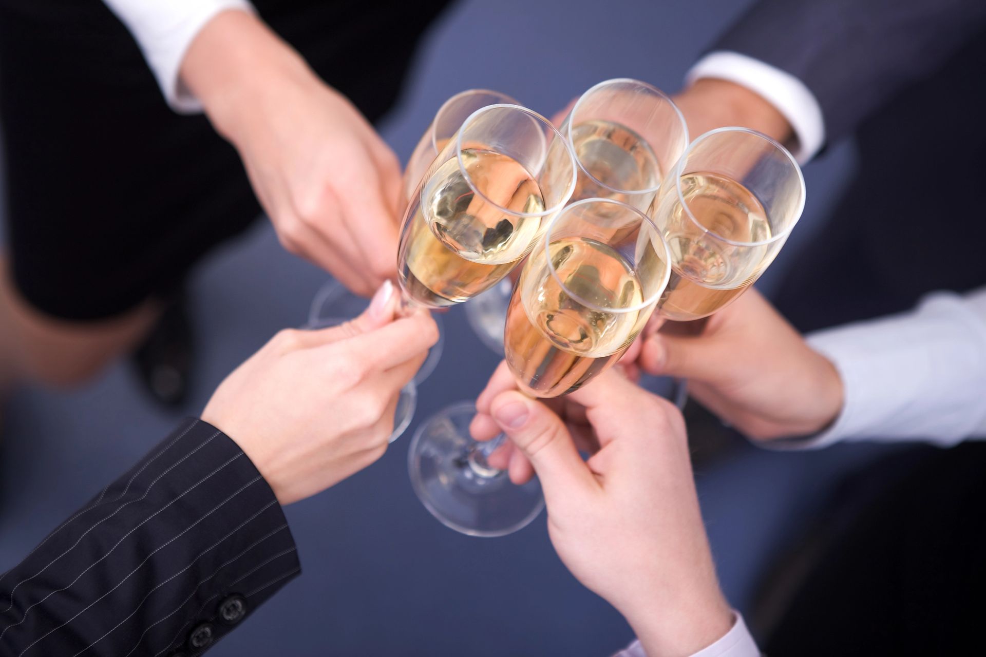 Quattro persone in abiti da lavoro brindano con calici di champagne su uno sfondo neutro.