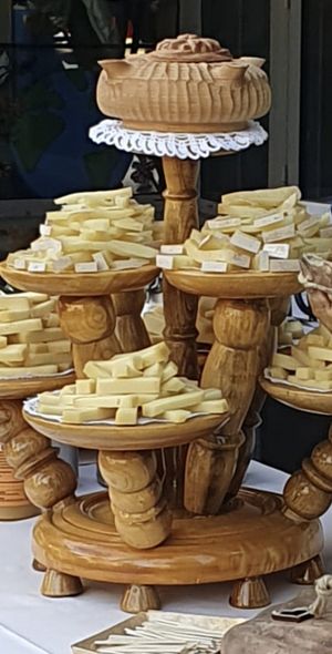 Alzata di legno a più livelli con vari tagli di formaggio, sormontata da una ciotola decorativa in legno, su un tavolo bianco.