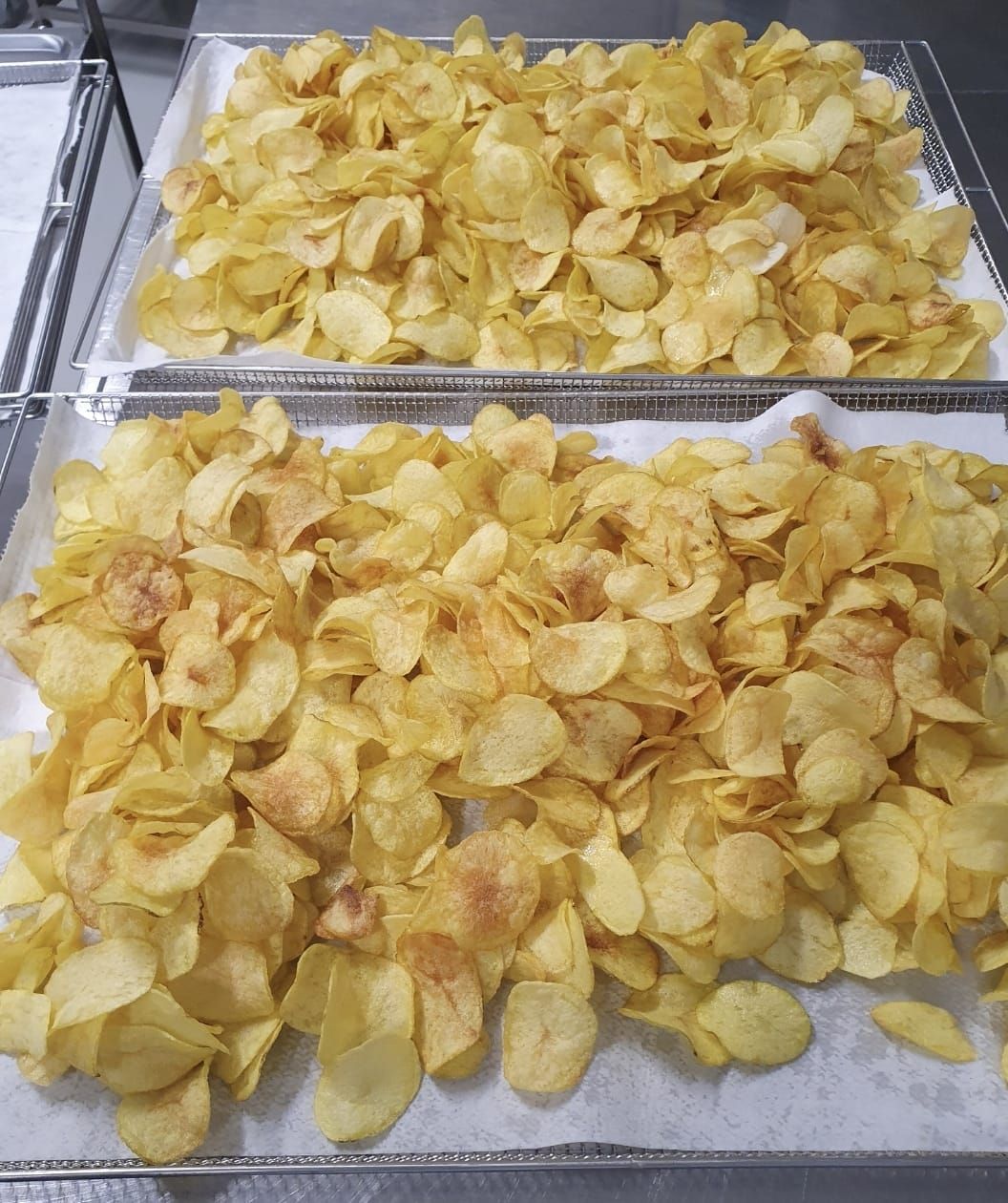 In una cucina, due grandi vassoi di metallo colmi di patatine fritte sottili e dorate, adagiate su fogli di carta.