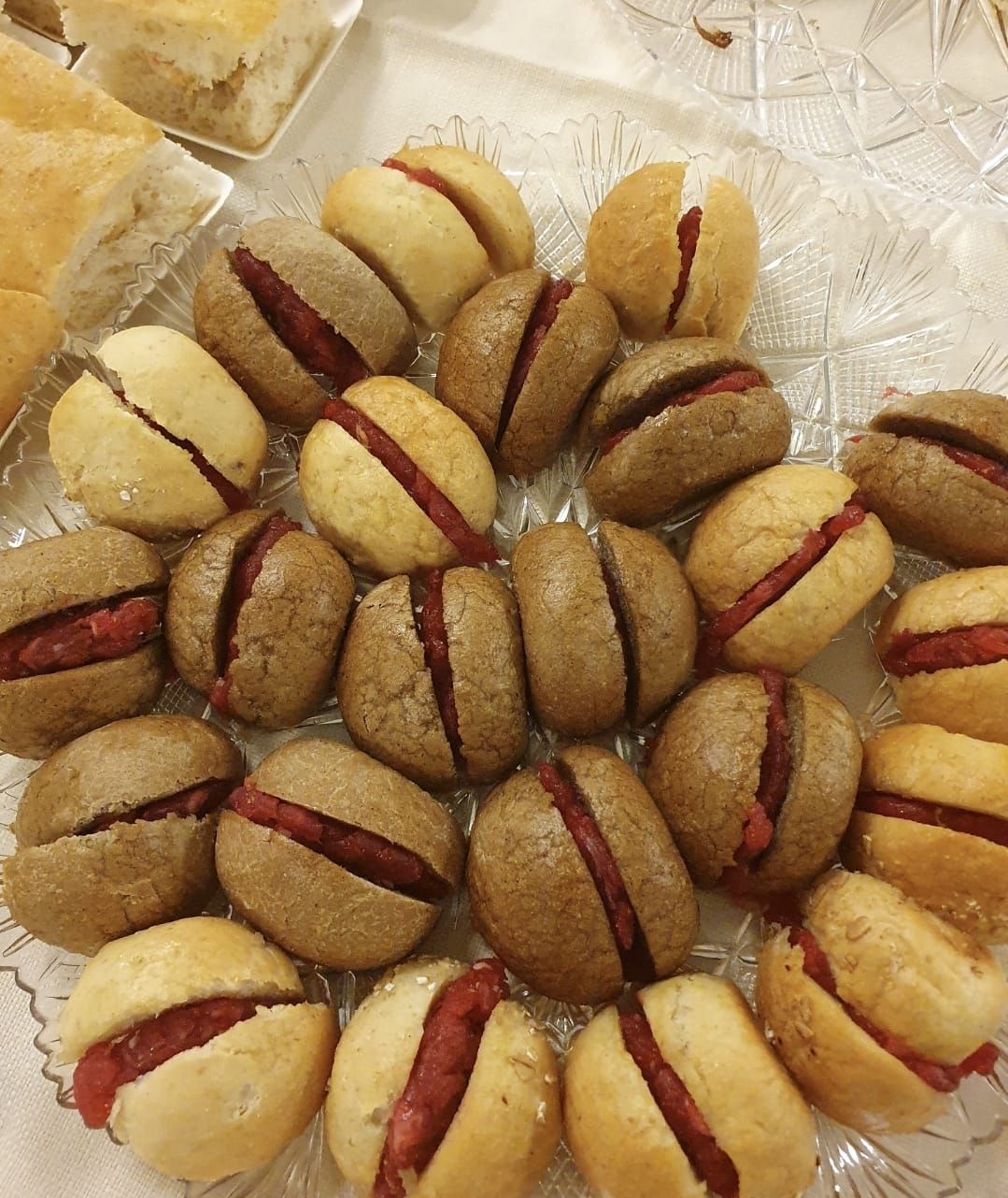 Un vassoio di panini rotondi di colore marrone chiaro e scuro, ciascuno tagliato a metà e farcito con una crema spalmabile di un rosso acceso.