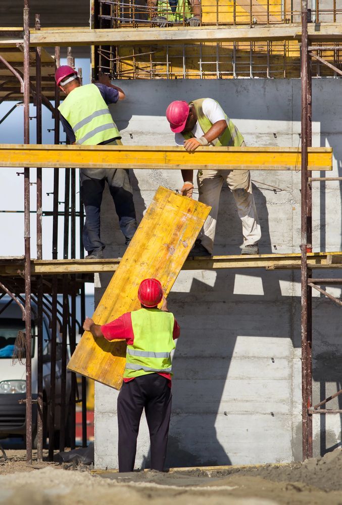Operai edili con caschi e giubbotti di protezione installano casseforme di legno sulle impalcature.