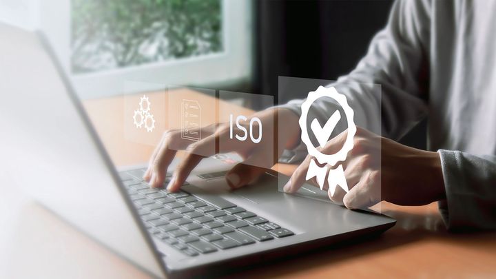 Persona che digita su un computer portatile con un badge di garanzia della qualità ISO sovrapposto.