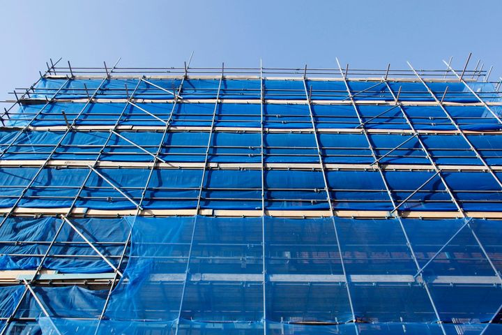 Le impalcature ricoprono la facciata dell'edificio, reti di sicurezza blu, cielo terso sopra.