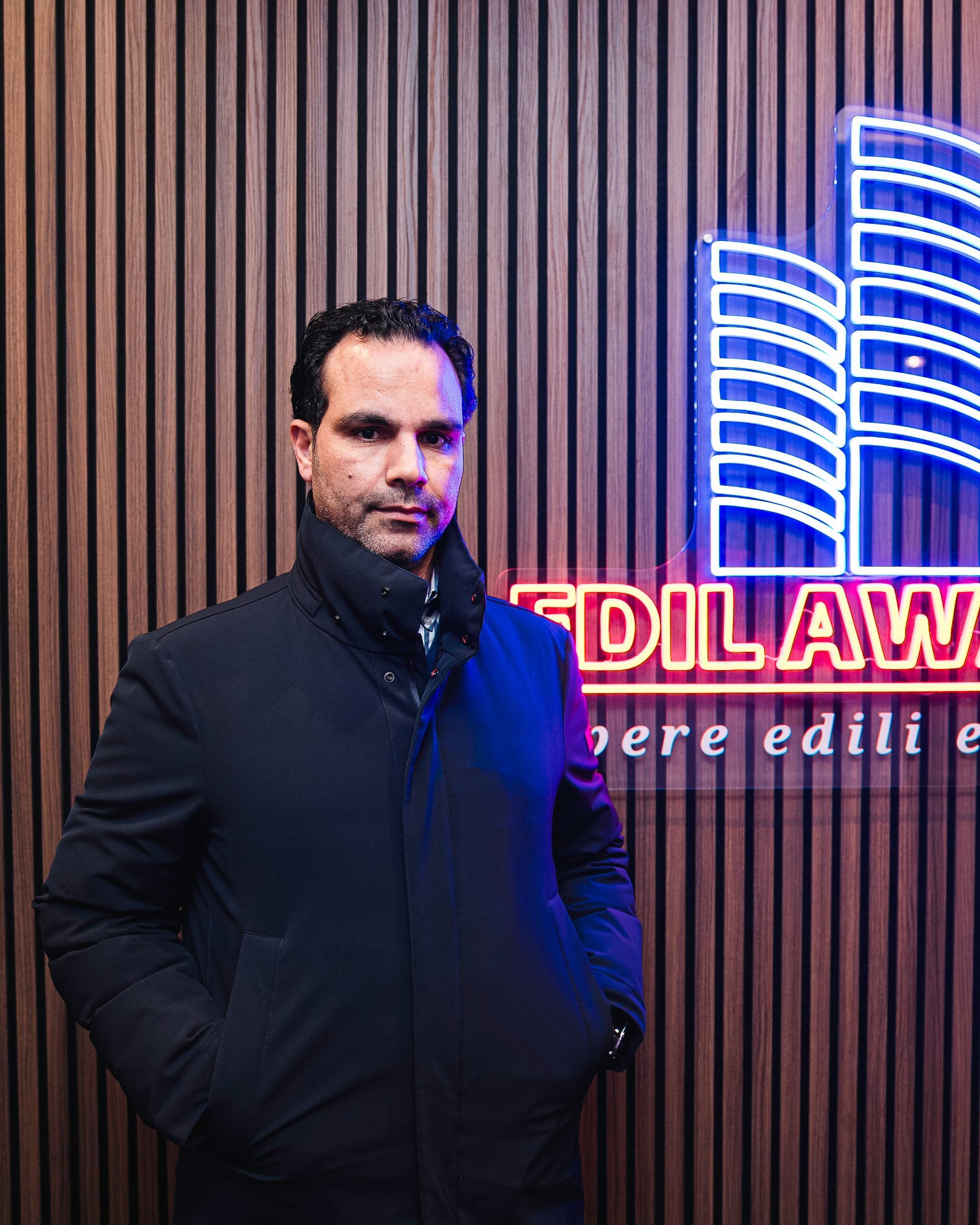 Un uomo con una giacca blu è in piedi in un ufficio con le braccia incrociate e guarda la telecamera.