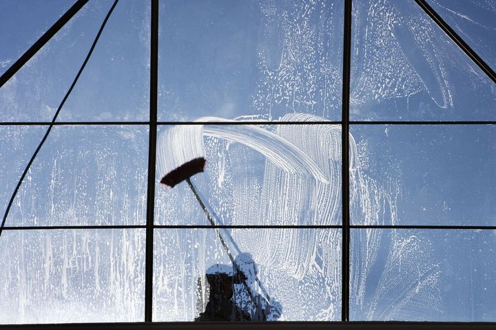 Finestra in fase di pulizia; un tergivetro rimuove l'acqua saponata, rivelando un cielo limpido.