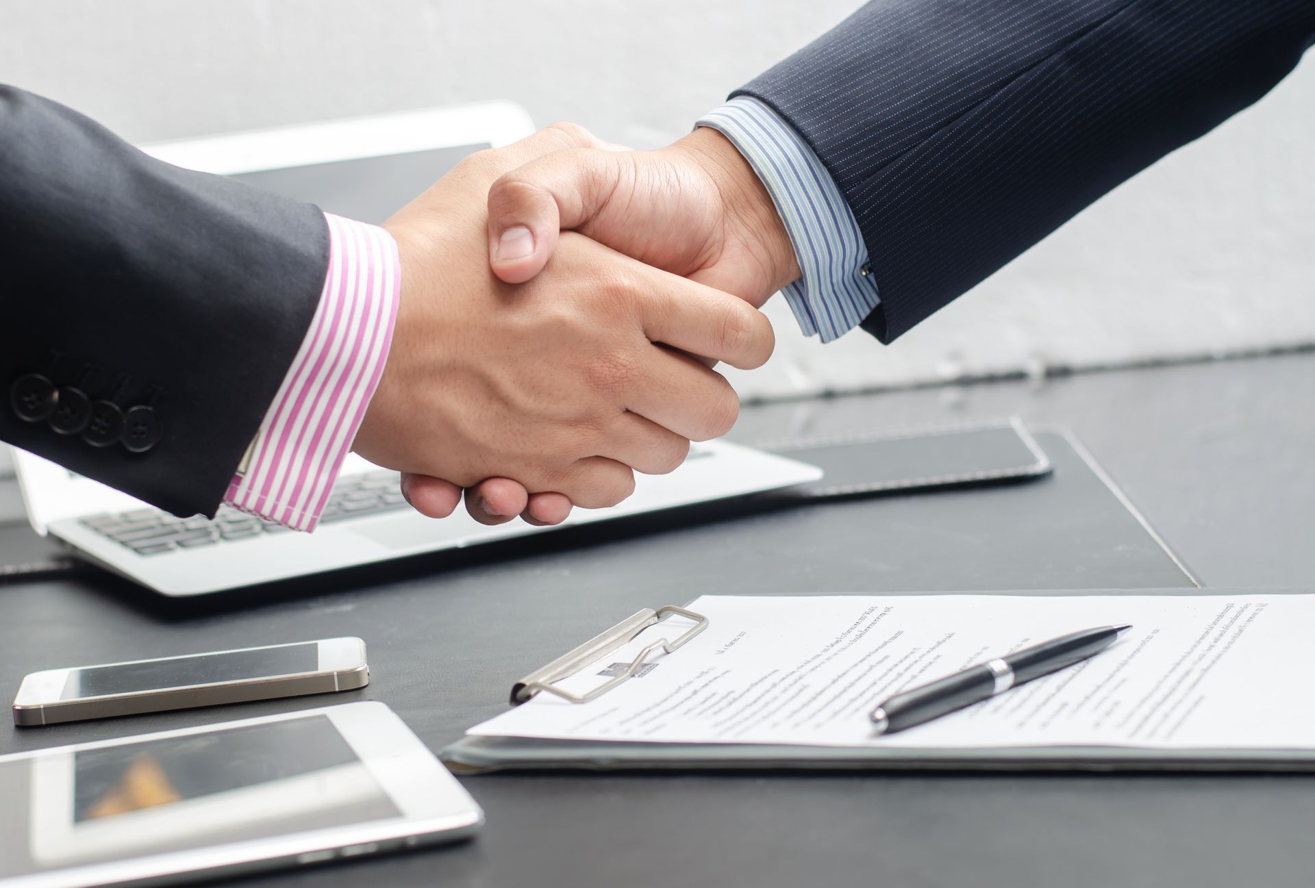 Due uomini d'affari si stringono la mano per leggere un contratto su una scrivania.