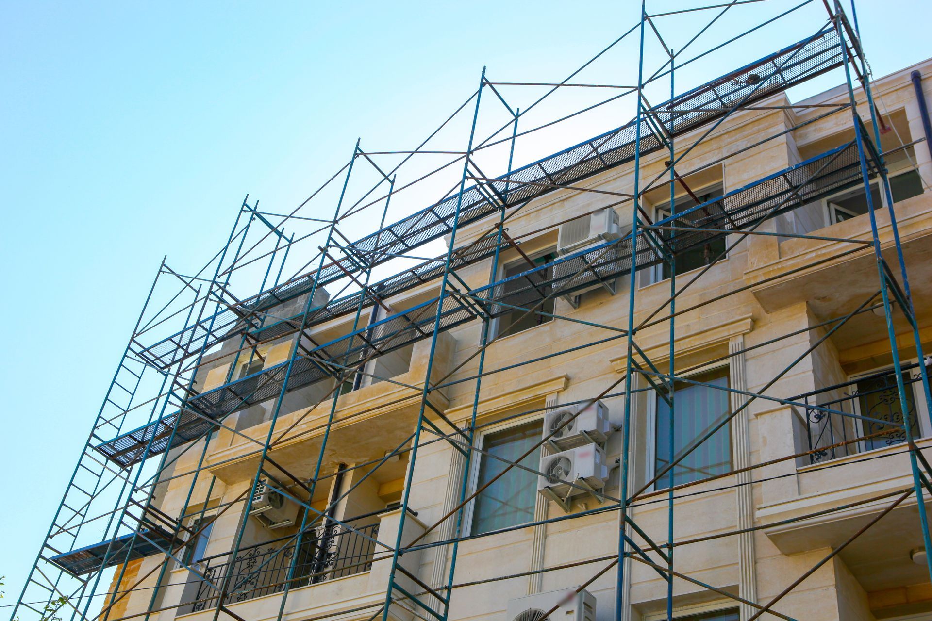 Un'impalcatura ricopre un edificio a più piani, probabilmente per lavori di ristrutturazione o riparazione. Sfondo cielo azzurro.