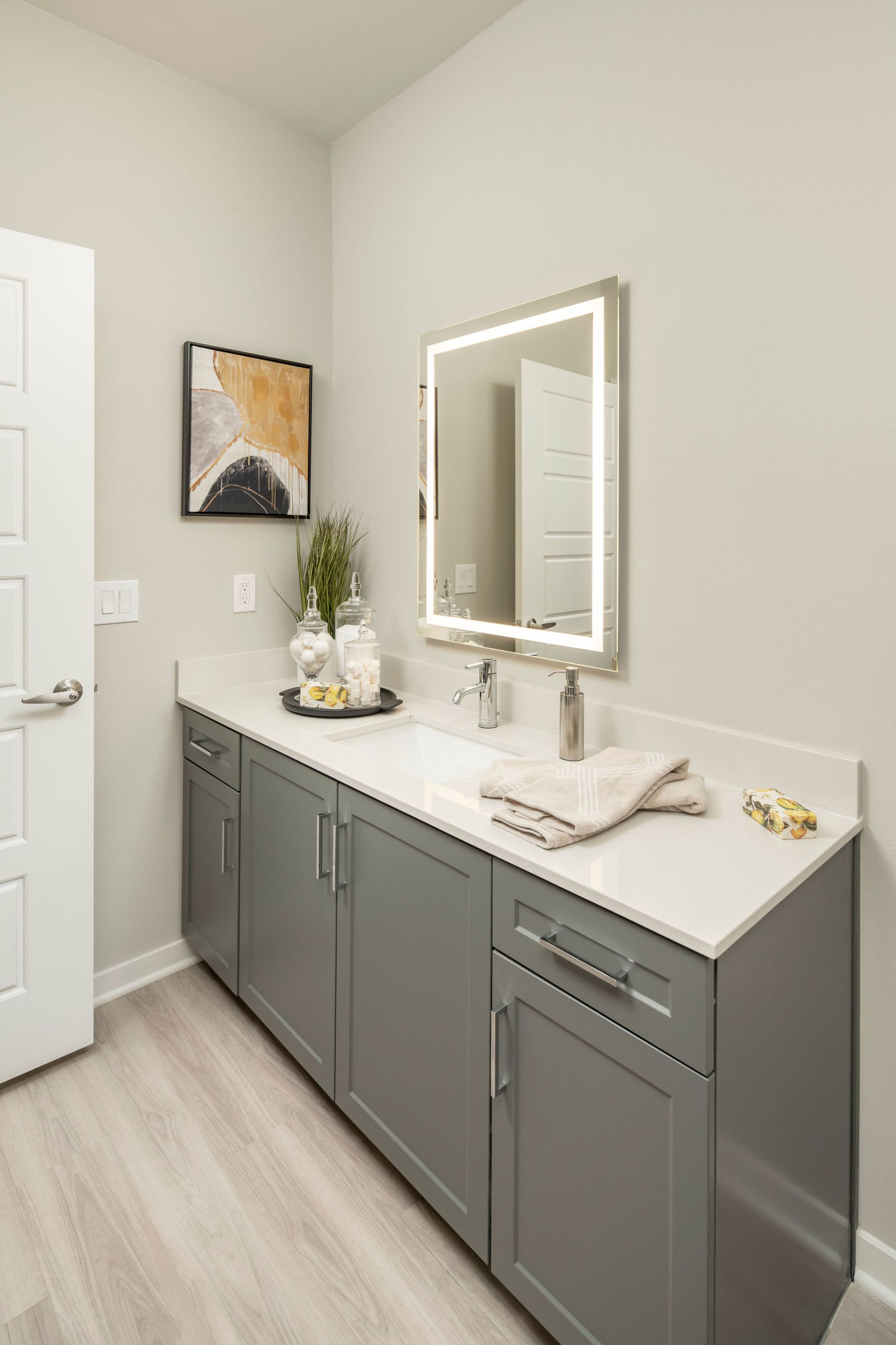 Modern bathroom vanity with gray cabinetry, white countertop, and backlit mirror.