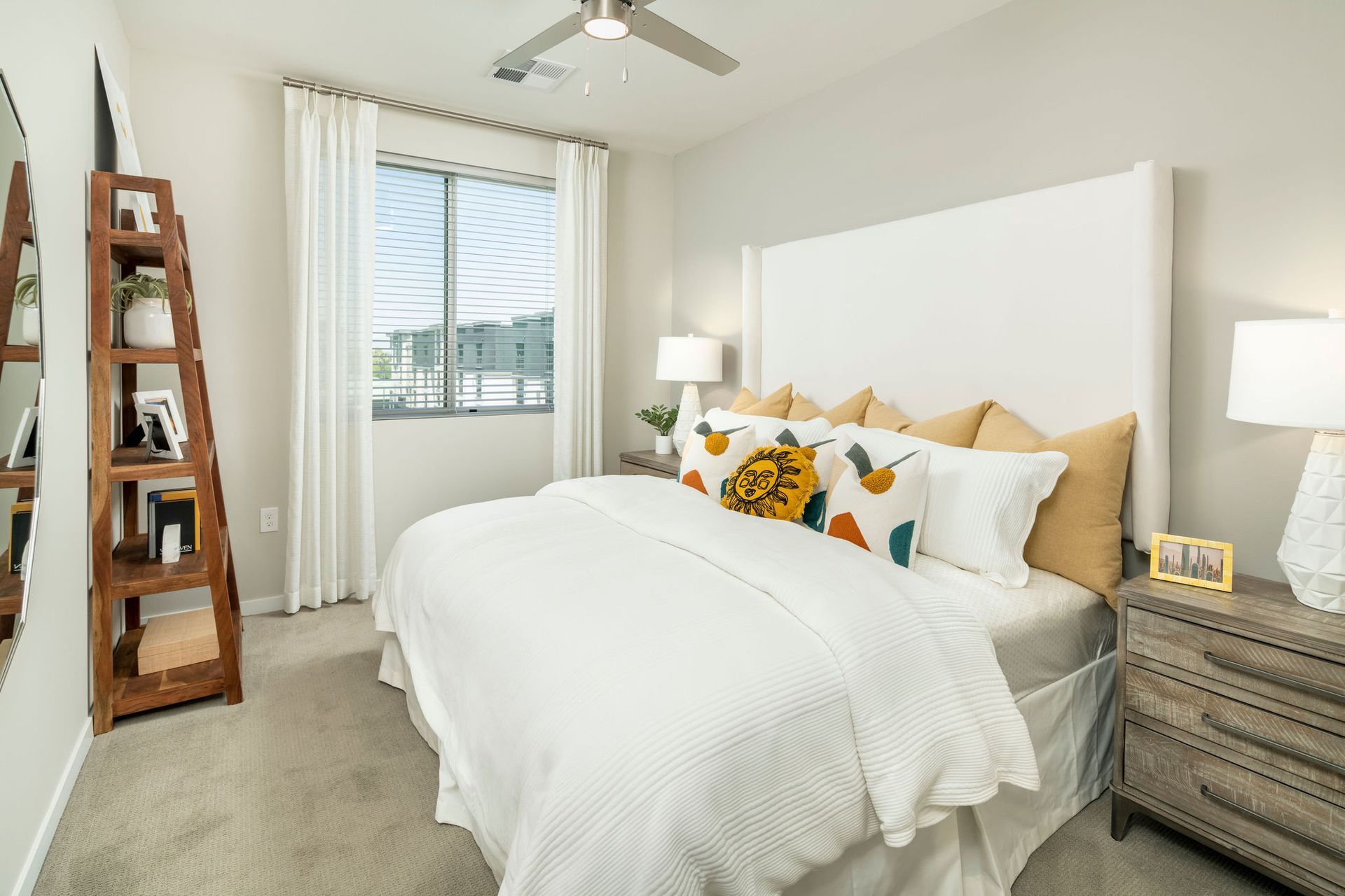 Bedroom in a modern apartment with a white bed, headboard, nightstands, and a window with sheer curtains.