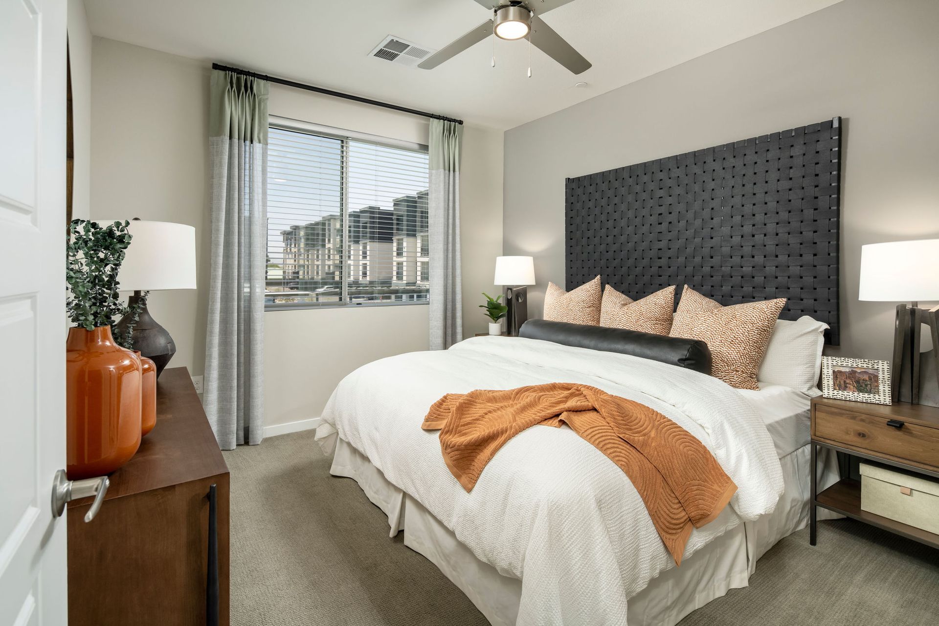 Bedroom in a modern apartment with a large dark headboard, white bedding, and neutral decor.