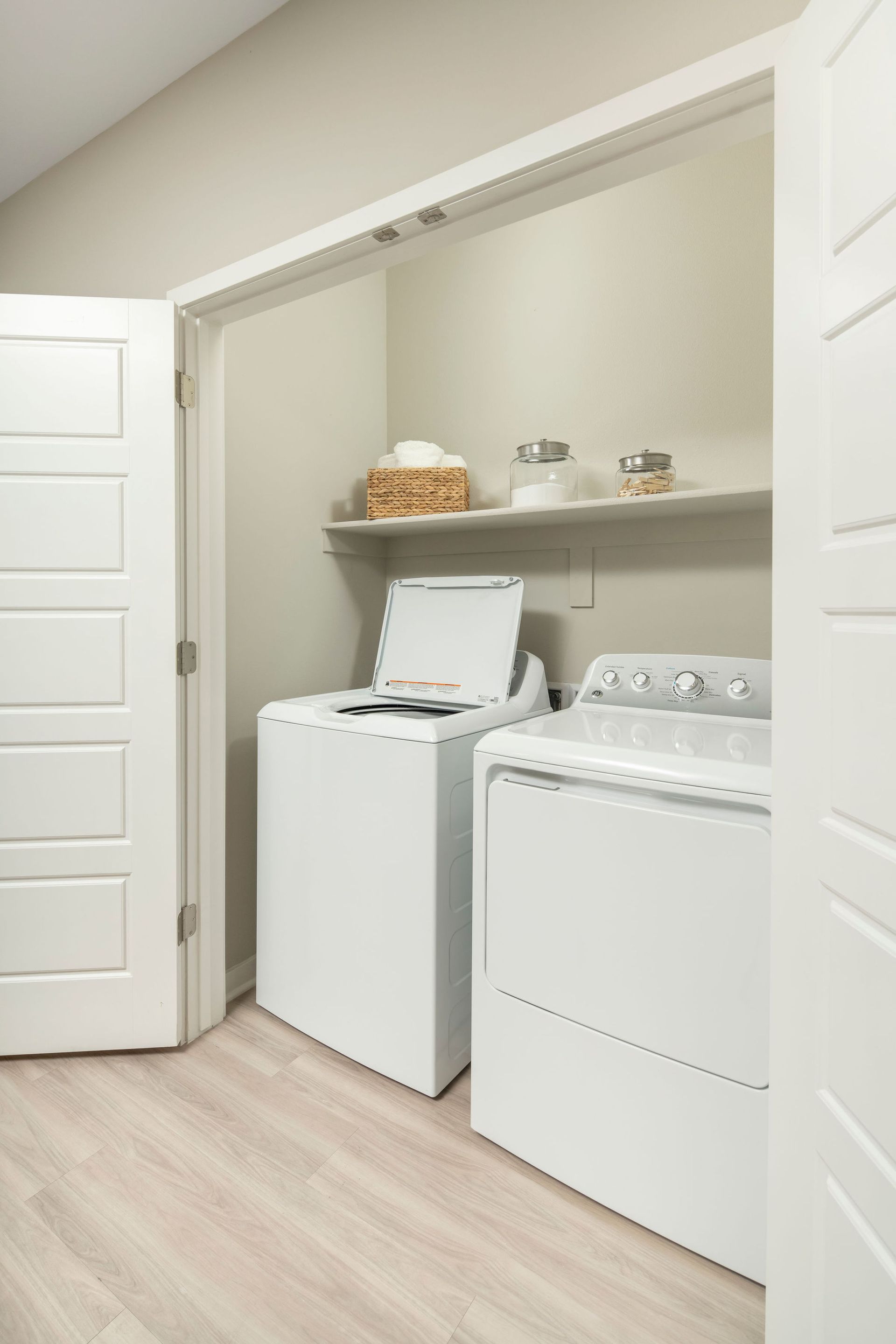 Laundry closet with a top-loading washer and front-loading dryer, and a shelf above.