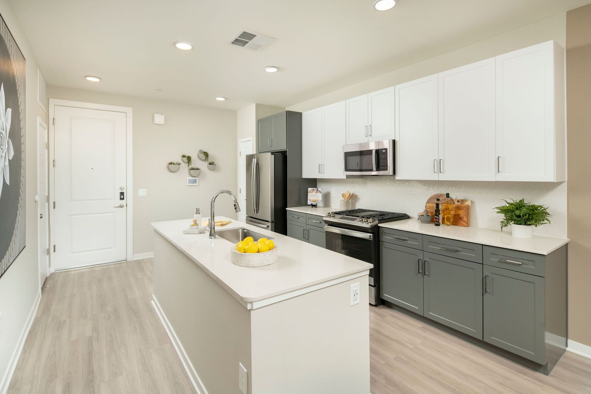 Modern apartment kitchen with white upper cabinets, gray lower cabinets, and stainless steel appliances.
