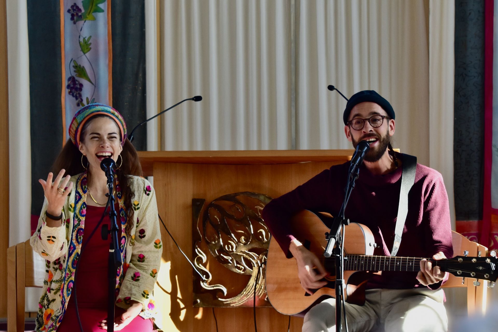 Two people singing into mics at a synagogue. One is playing a guitar.