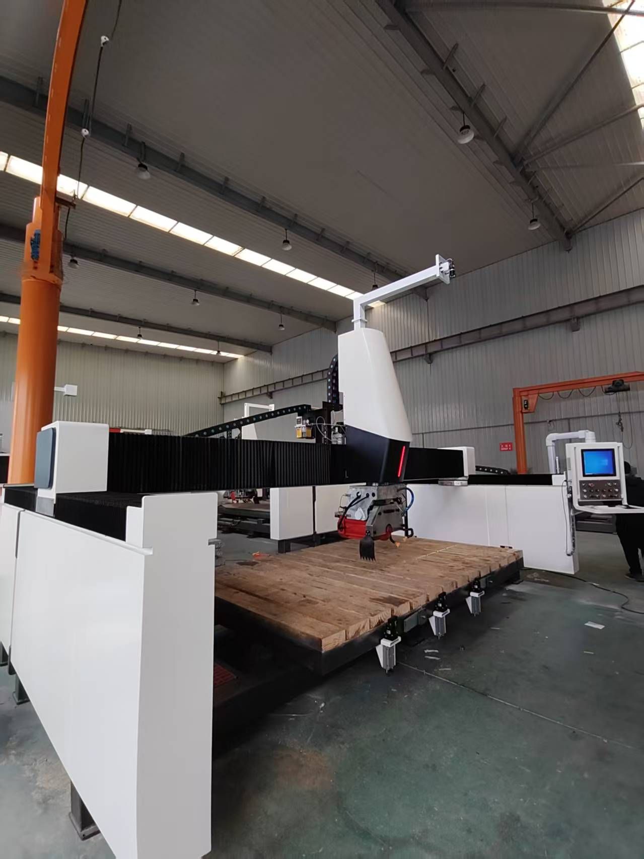 Large industrial CNC machine with white and black components in a warehouse.
