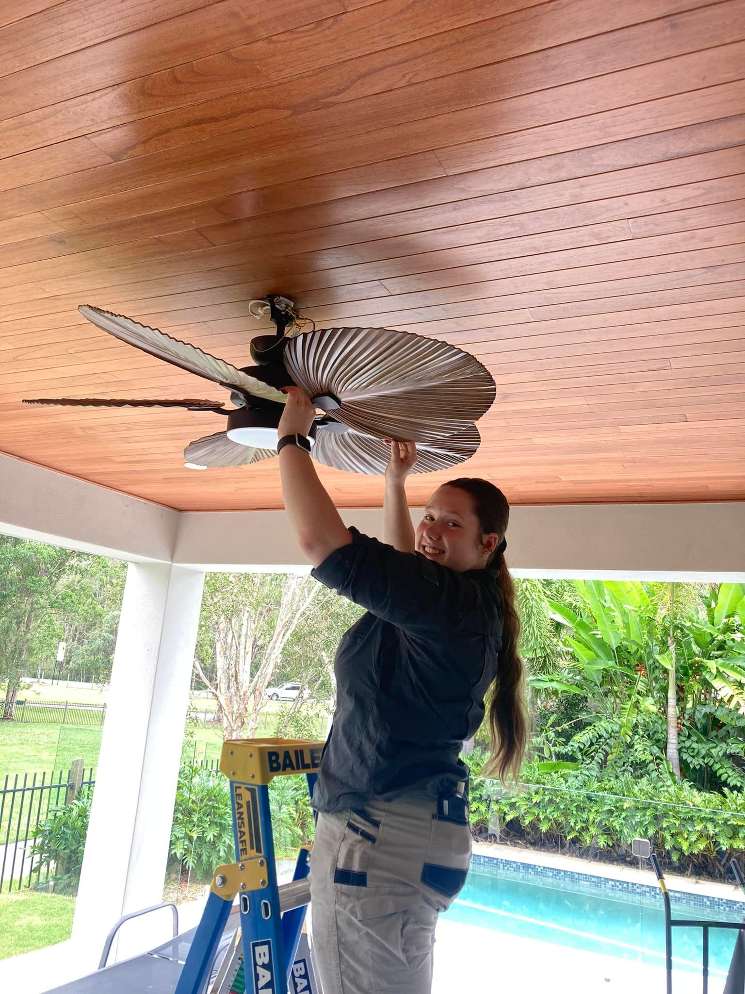 A woman is standing on a ladder fixing a ceiling fan. — Short Stop Electrical in Nerang, QLD
